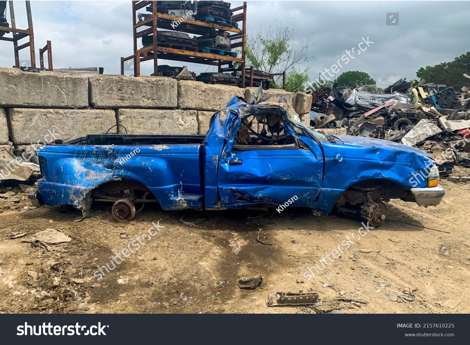 Side view of damaged blue pickup without wheels on the junkyard after car accident on a road, cemetery of cars, recycling broken automobiles #2157610225