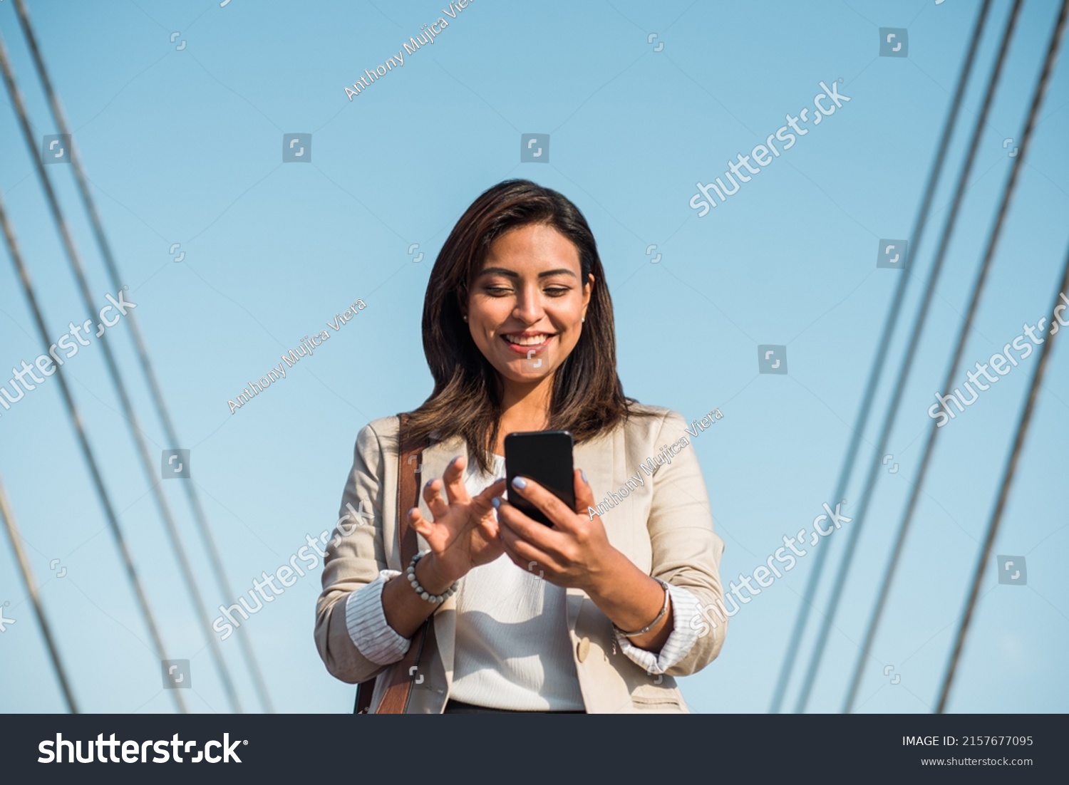 A happy elegant young woman stands and uses her phone to type an important message. A businesswoman using technologies outdoors. #2157677095