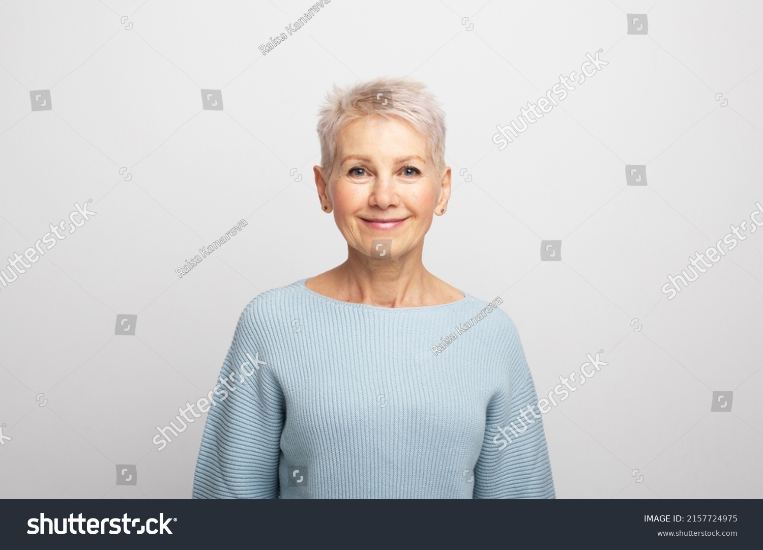 Elderly beautiful woman with a short pixie haircut in a blue sweater on a gray background #2157724975