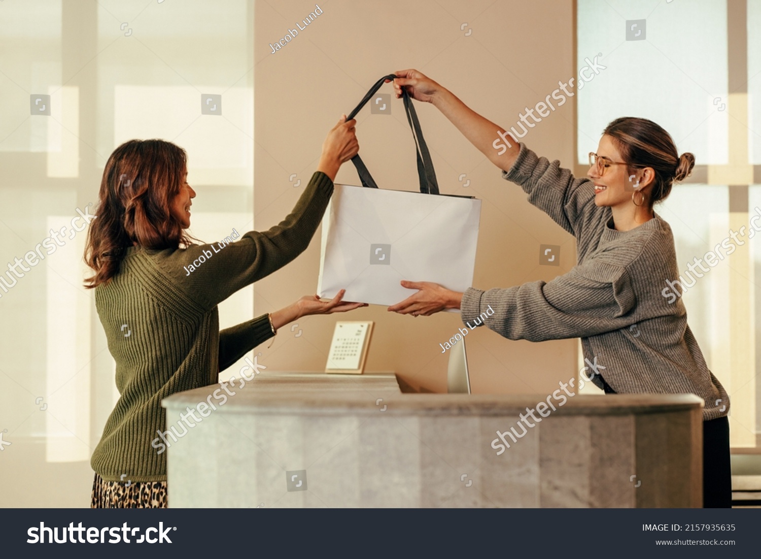 Clothing store owner handing a female customer a shopping bag with her clothing items. Happy small business owner assisting an online shopper during an in store collection. #2157935635