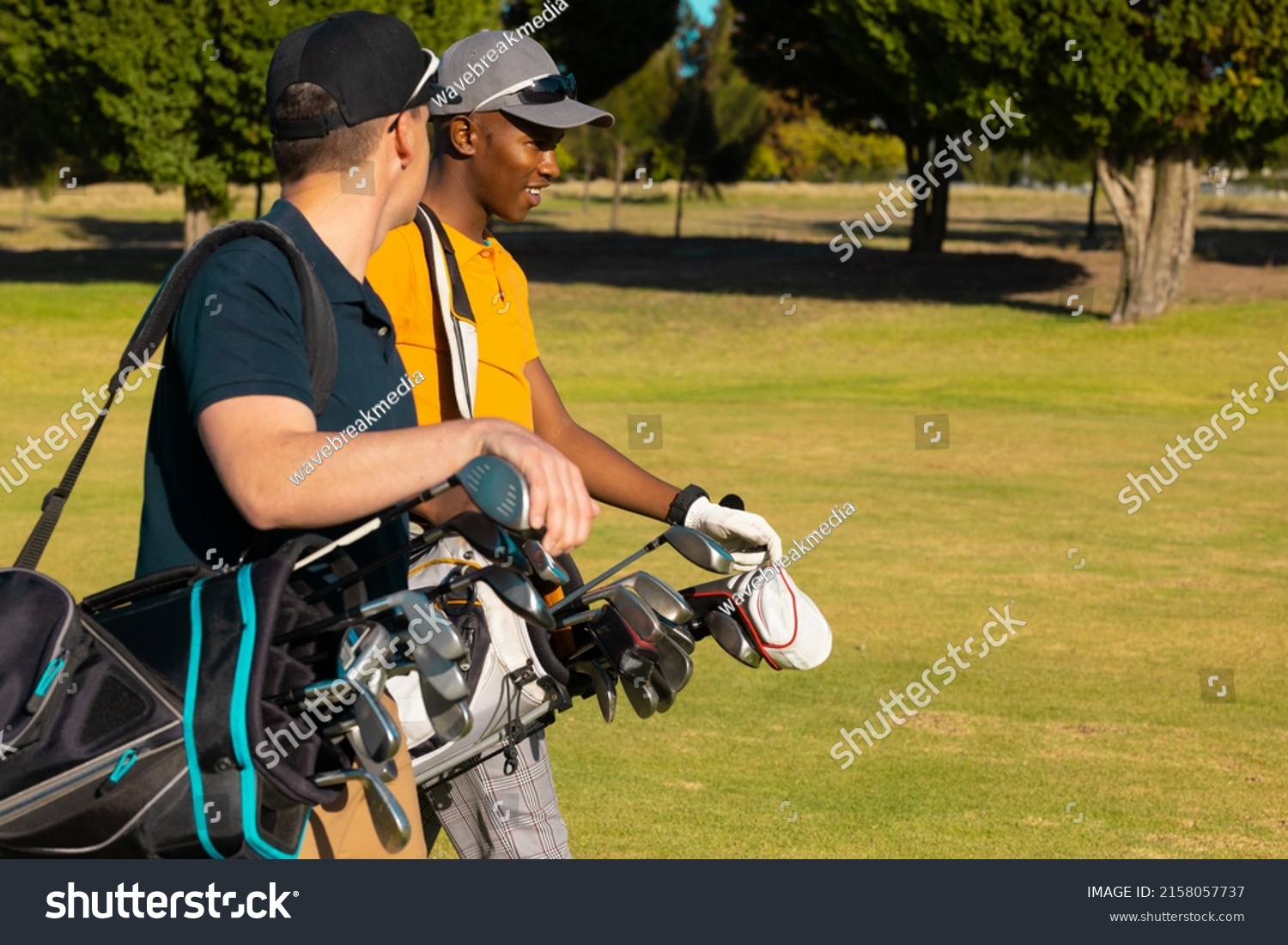 Side view of multiracial young male friends wearing caps with golf bags walking at golf course. summer, golf, unaltered, friendship, togetherness, nature, sport and weekend activities concept. #2158057737