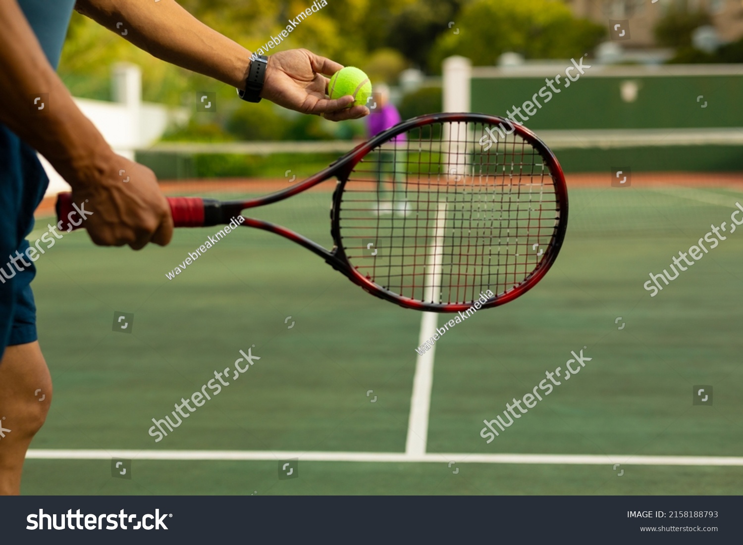 Midsection of biracial senior man holding racket serving tennis ball while playing at tennis court. unaltered, sport, competition, retirement, healthy and active lifestyle concept. #2158188793