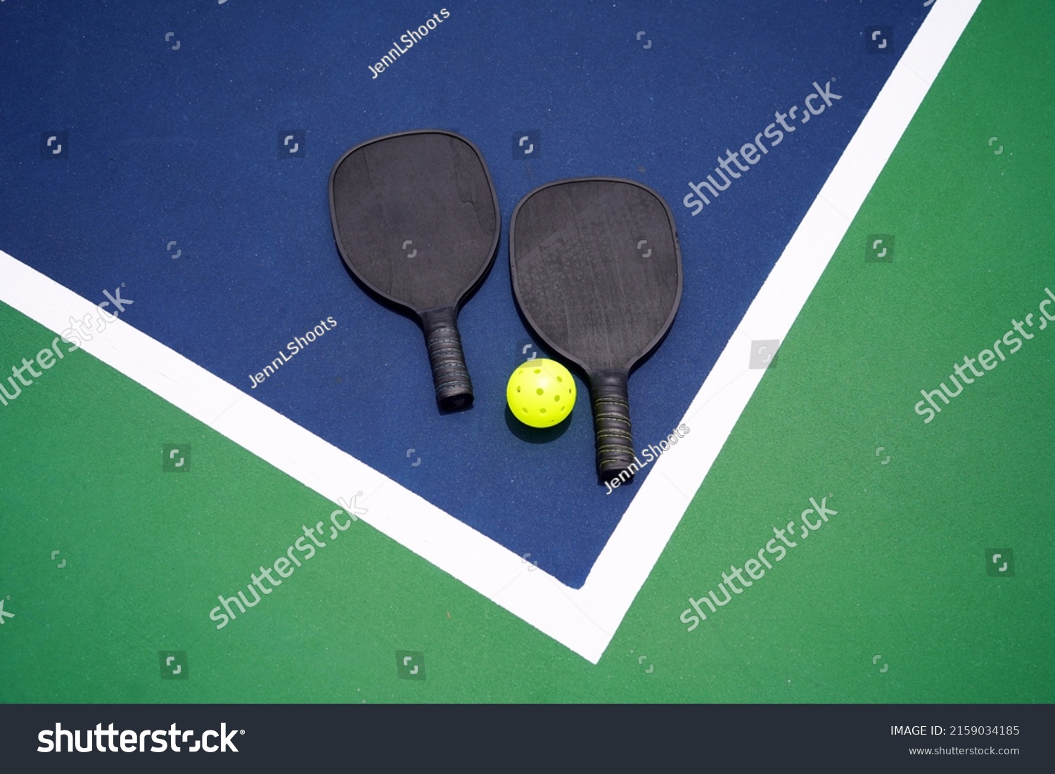 Two pickle ball paddles with a pickle ball on court.                           #2159034185