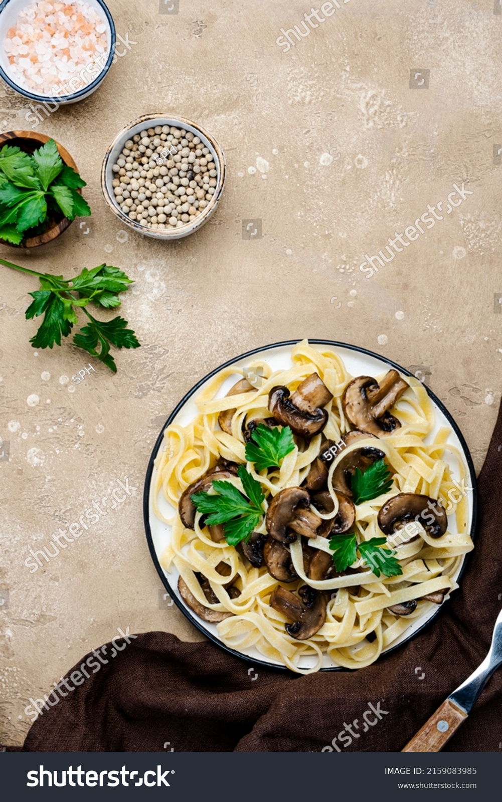 Cooked pasta with mushrooms with parsley on plate on beige stone kitchen table background, top view. Vegan cooking and eating, italian cuisine recipe #2159083985