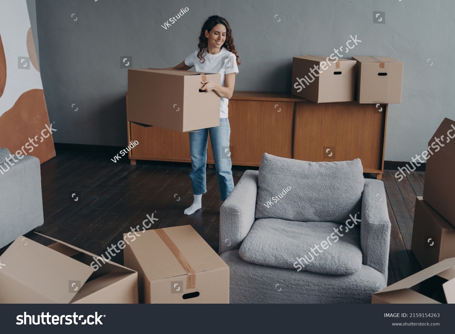 Hispanic girl is holding box and leaving apartment. Happy young woman relocates alone. Single lady moves. Real estate purchase, mortgage, delivery service ordering concept. #2159154263
