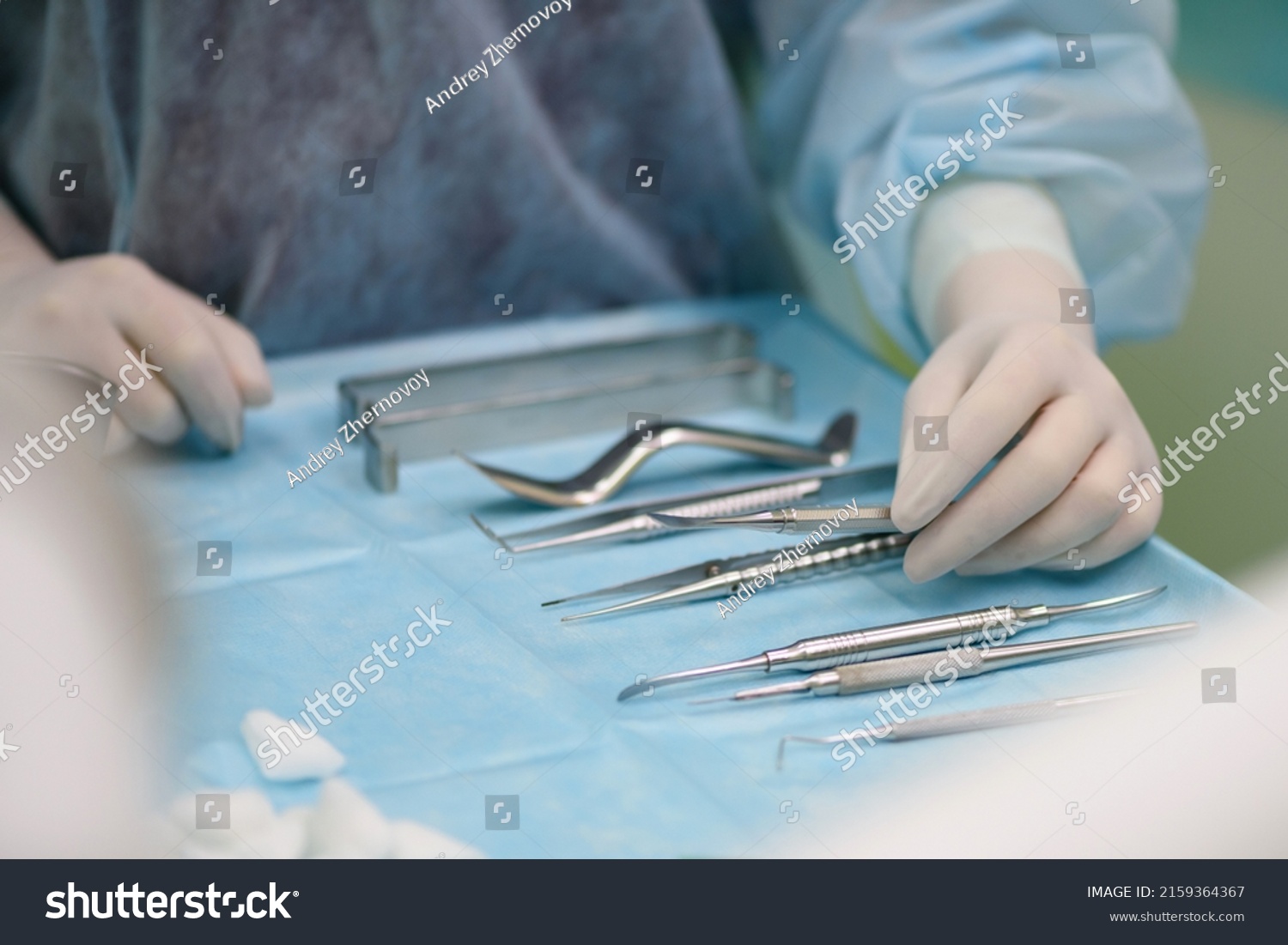 Surgical instruments in the operating room. A nurse in a surgical suit and gloves is preparing for a tooth implant operation.
Dental probe, tweezers, scalpel, needle holder, rasps on instrument table. #2159364367