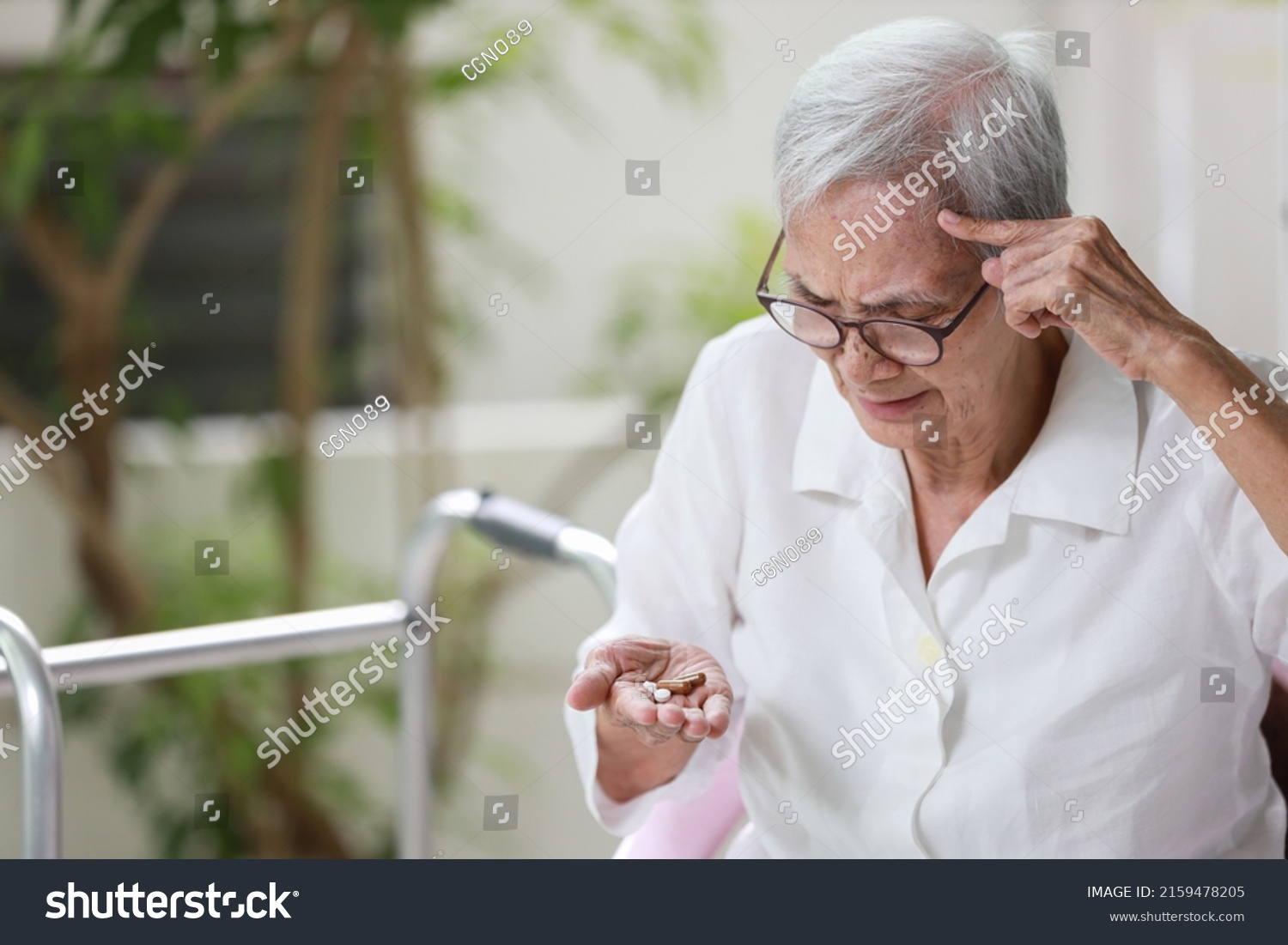 Asian senior patient with Alzheimer's disease or dementia,look at the pills capsules on her palm,trying to think,confused,old elderly people forget to take the medication,fail to remember or amnesia #2159478205