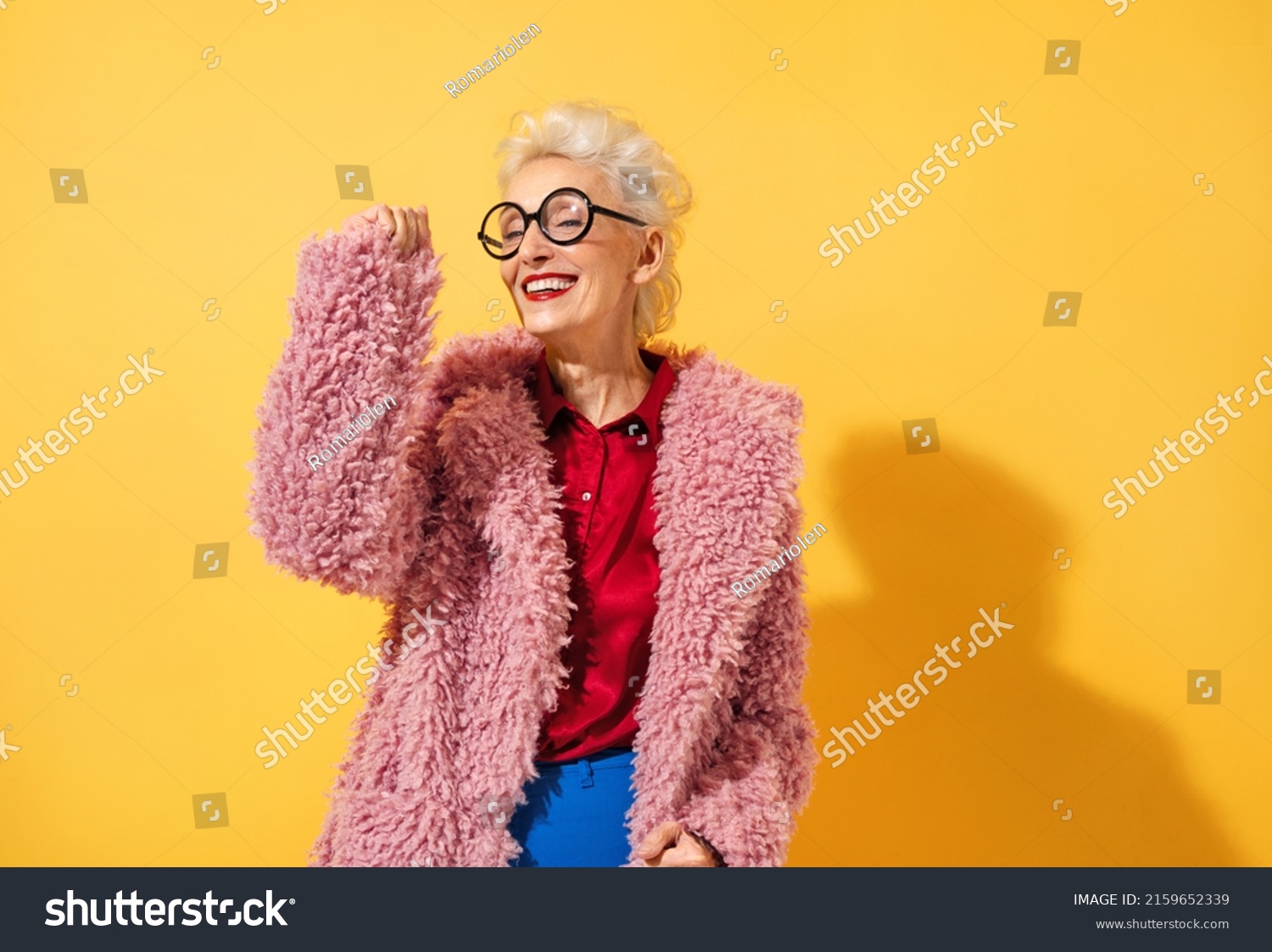 Happy and playful mature woman dancing, smiling and having fun. Photo of elderly woman above 70 years old in stylish outfit on yellow background #2159652339