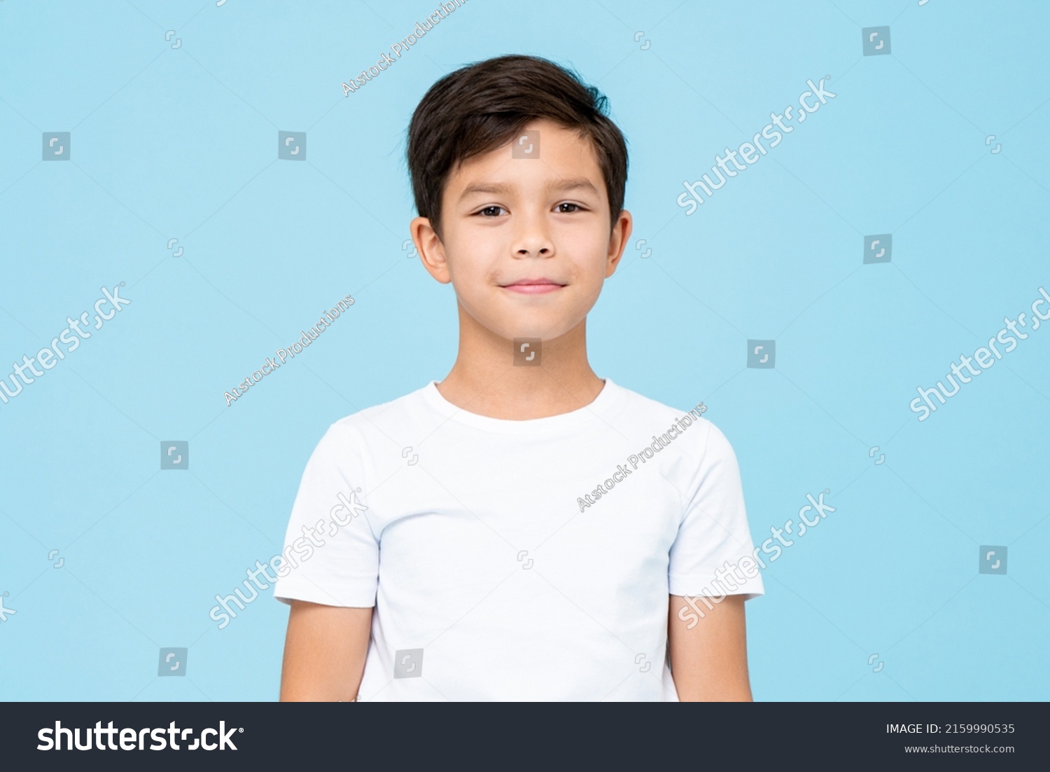 Cute smiling boy in plain white t shirt looking at camera in isolated studio light blue color background #2159990535