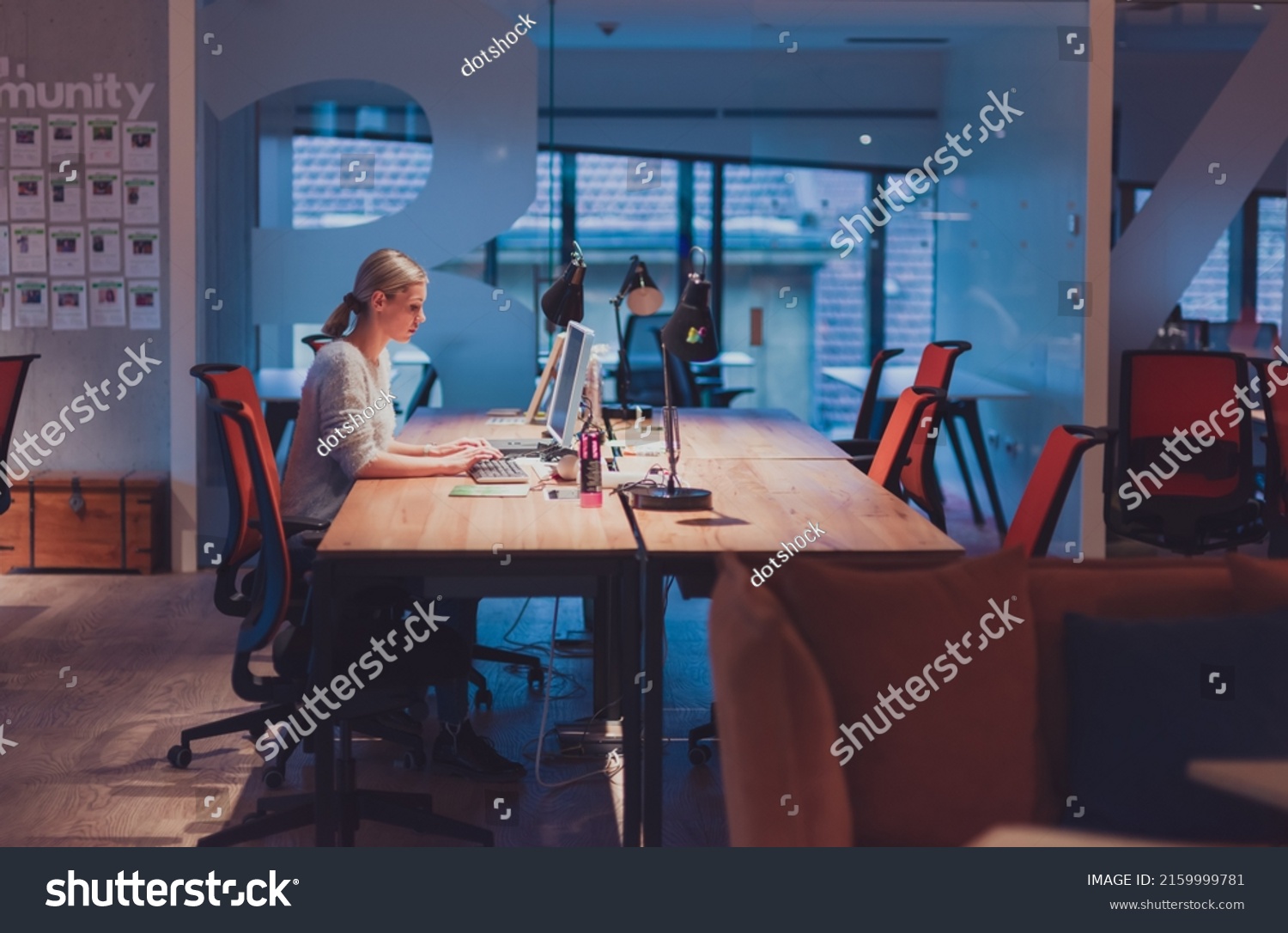 business woman working overtime alone at his desk on a desktop computer in an open space modern coworking office #2159999781