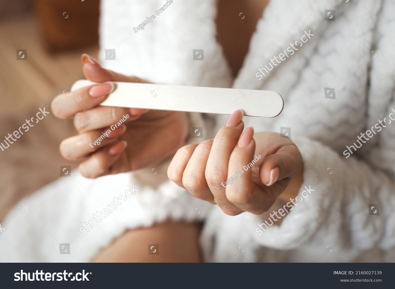 Closeup photo of young womans hand makes herself a manicure, files her nails with a nail file. Personal hygiene #2160027139