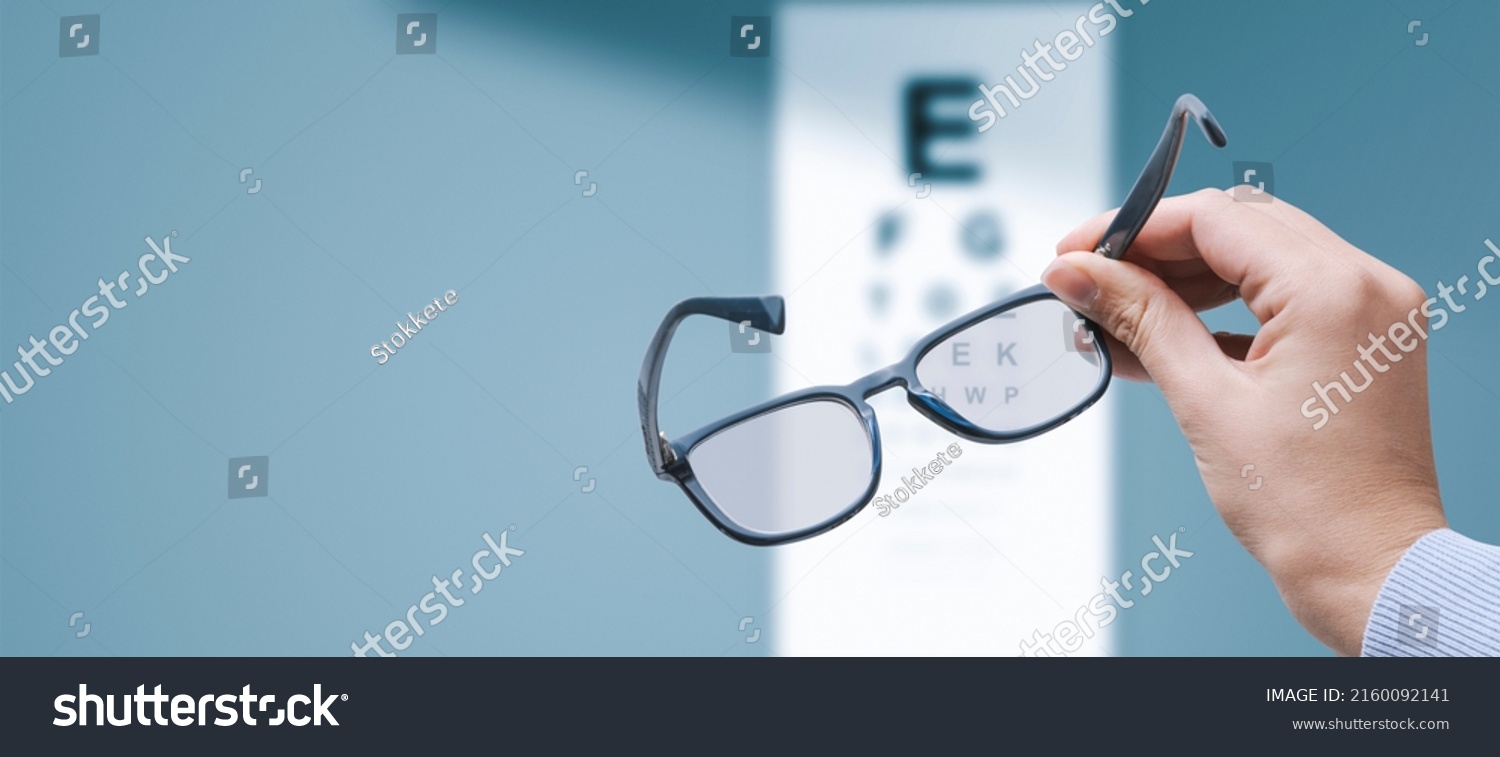 Professional optometrist holding glasses and eye chart in the background, eyesight and vision problems concept, copy space #2160092141