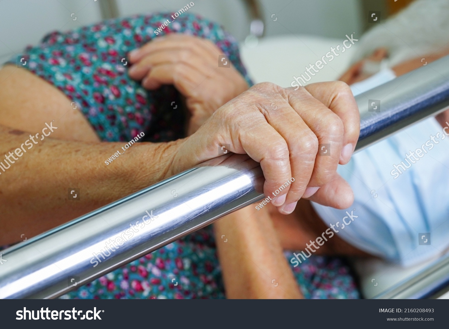 Asian elder senior woman patient holding bed rail while lie down with hope waiting her family in hospital. #2160208493
