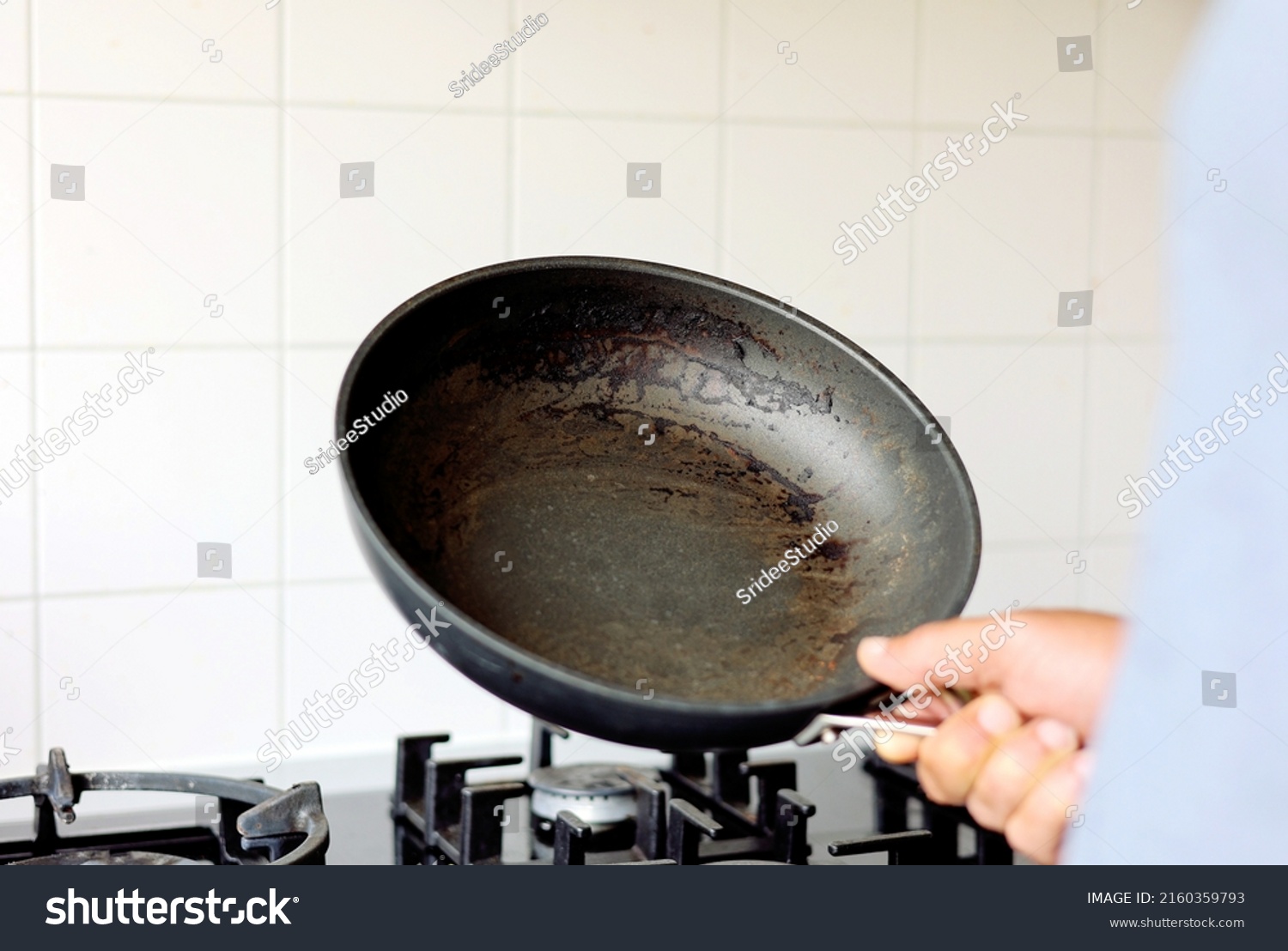 Close up man hand holding dirty  burnt food unclean able stain on the pan in the kitchen. #2160359793