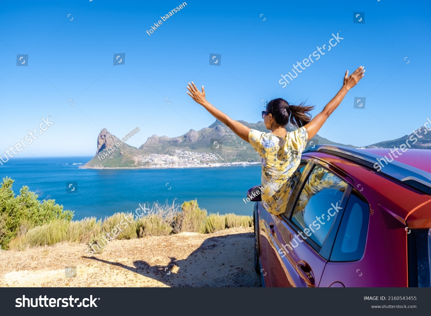 woman outside car window road trip with hands up, car at Chapmans Peak Drive in Cape Town South Africa looking out over the ocean.  #2160543455