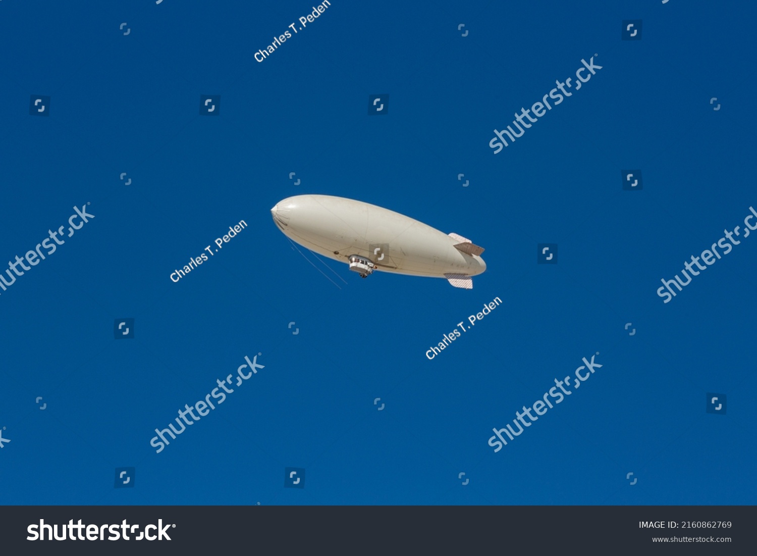 A white blimp, airship, or dirigible flying in blue sky. Close up detail of an unmarked zeppelin like flying vehicle. Flying high above in clear skies.   #2160862769