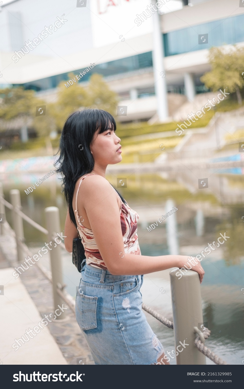 A fashionable woman with a a spaghetti strap top and denim skirt. A female with broad shoulders, a small bust and rectangular body shape. #2161329985