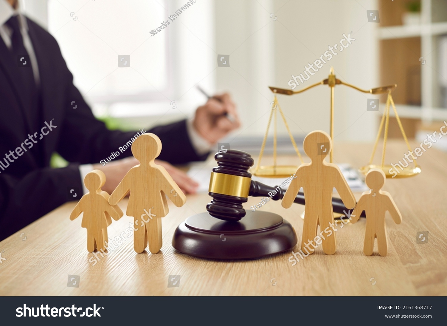 Gavel, sound block and little wooden figures of parents and children placed on desk in courthouse up close, judge and scales of justice in background. Family law, court, divorce, child custody concept #2161368717