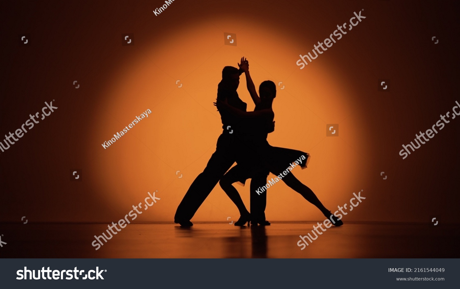Couple of dancers approach each other and begin to dance Argentine tango. Elements of latin ballroom dance in studio with orange brown background. Dark silhouettes. Slow motion ready, 4K at 59.94fps. #2161544049