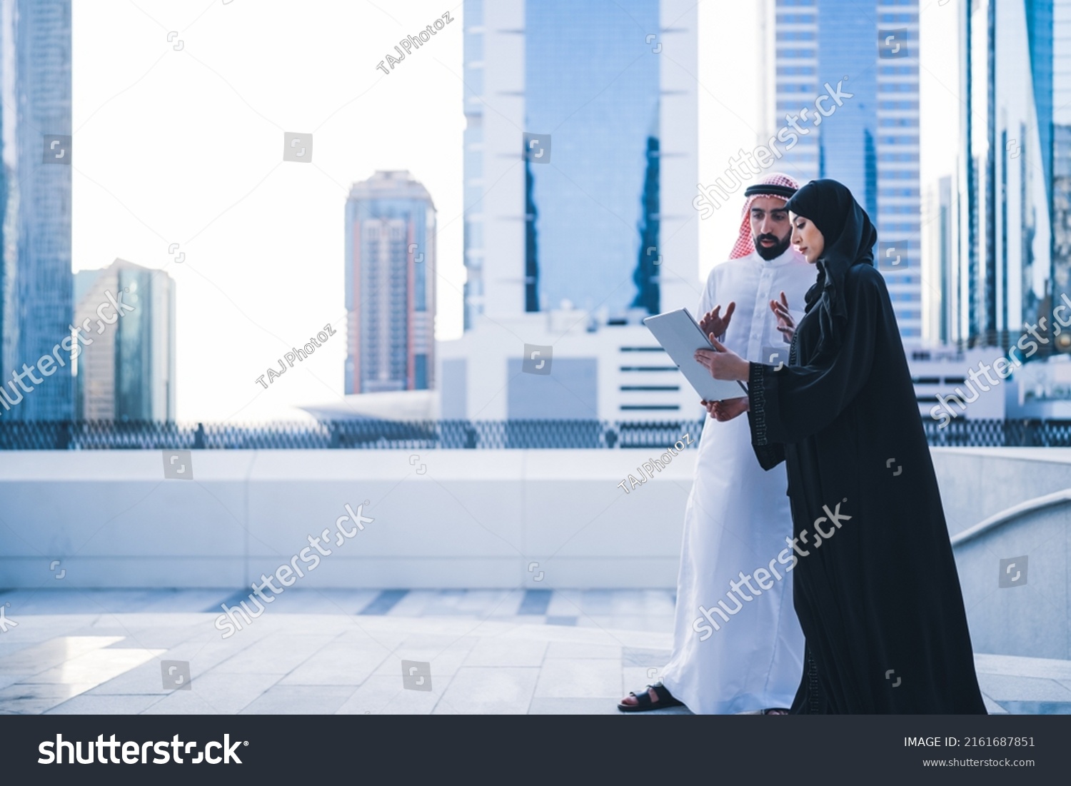Arab couples or colleagues working together on tablet or laptop wearing traditional clothes and abaya. Muslim employees Saudi or Emirati business woman and man #2161687851