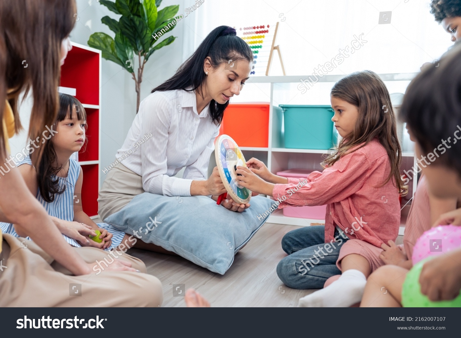 Caucasian beautiful young woman teacher teaching art to kids at school. Attractive Instructor master female explain and educate drawing and painting with student kindergarten pre school in classroom. #2162007107