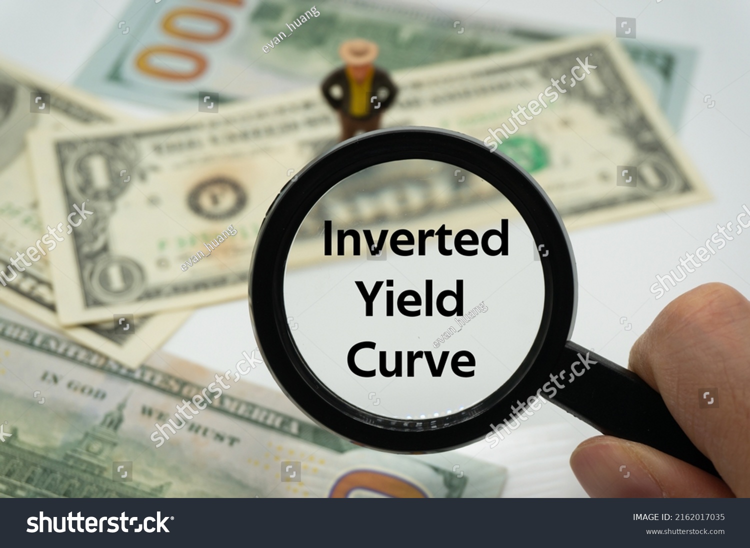 Inverted Yield Curve.Magnifying glass showing the words.Background of banknotes and coins.basic concepts of finance.Business theme.Financial terms. #2162017035