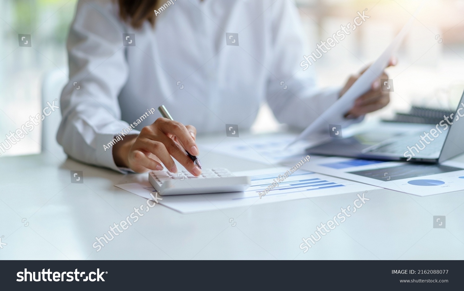 Close-up of businesswoman hands using a calculator to check company finances and earnings and budget. Business woman calculating monthly expenses, managing budget,  papers, loan documents, invoices. #2162088077