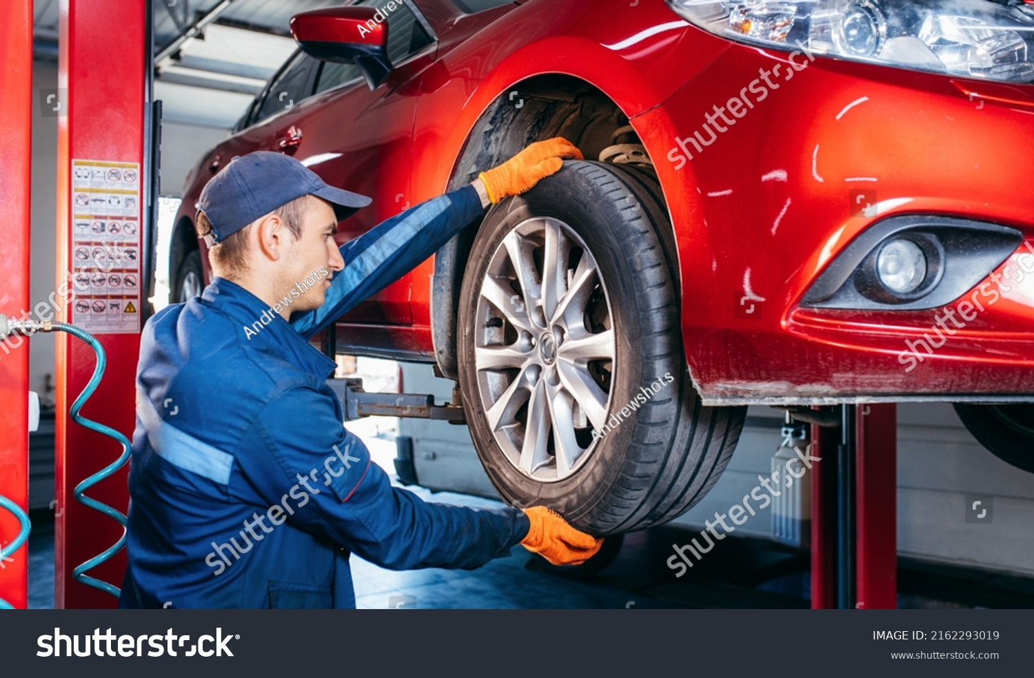 Expert specialist technician changes tires, tyres of lifted up car at auto service, wears uniform costume. #2162293019