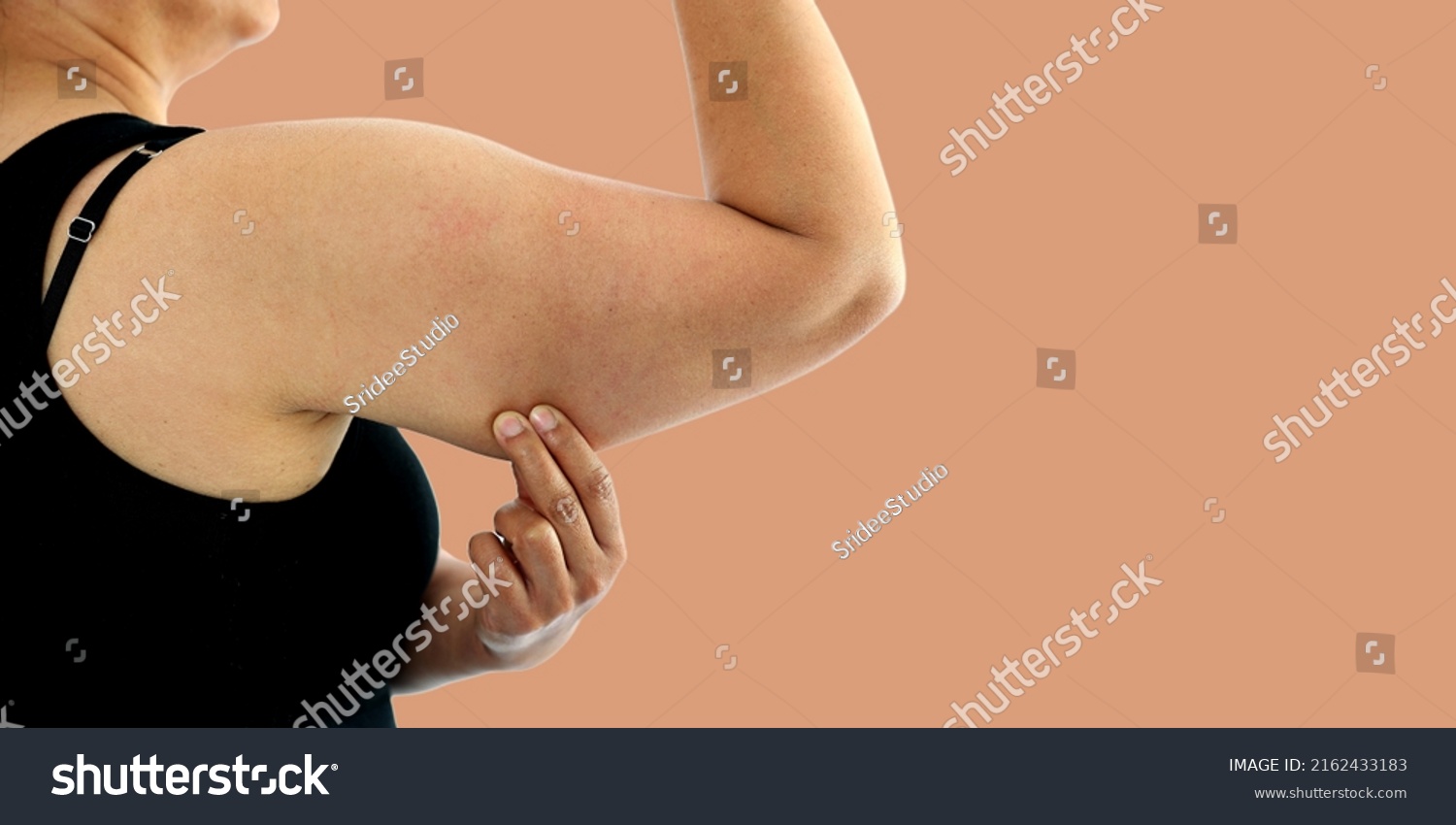 A young Asian woman grabbing skin on her upper arm with excess fat isolated on a white background. Pinching the loose and saggy muscles. Overweight concept #2162433183