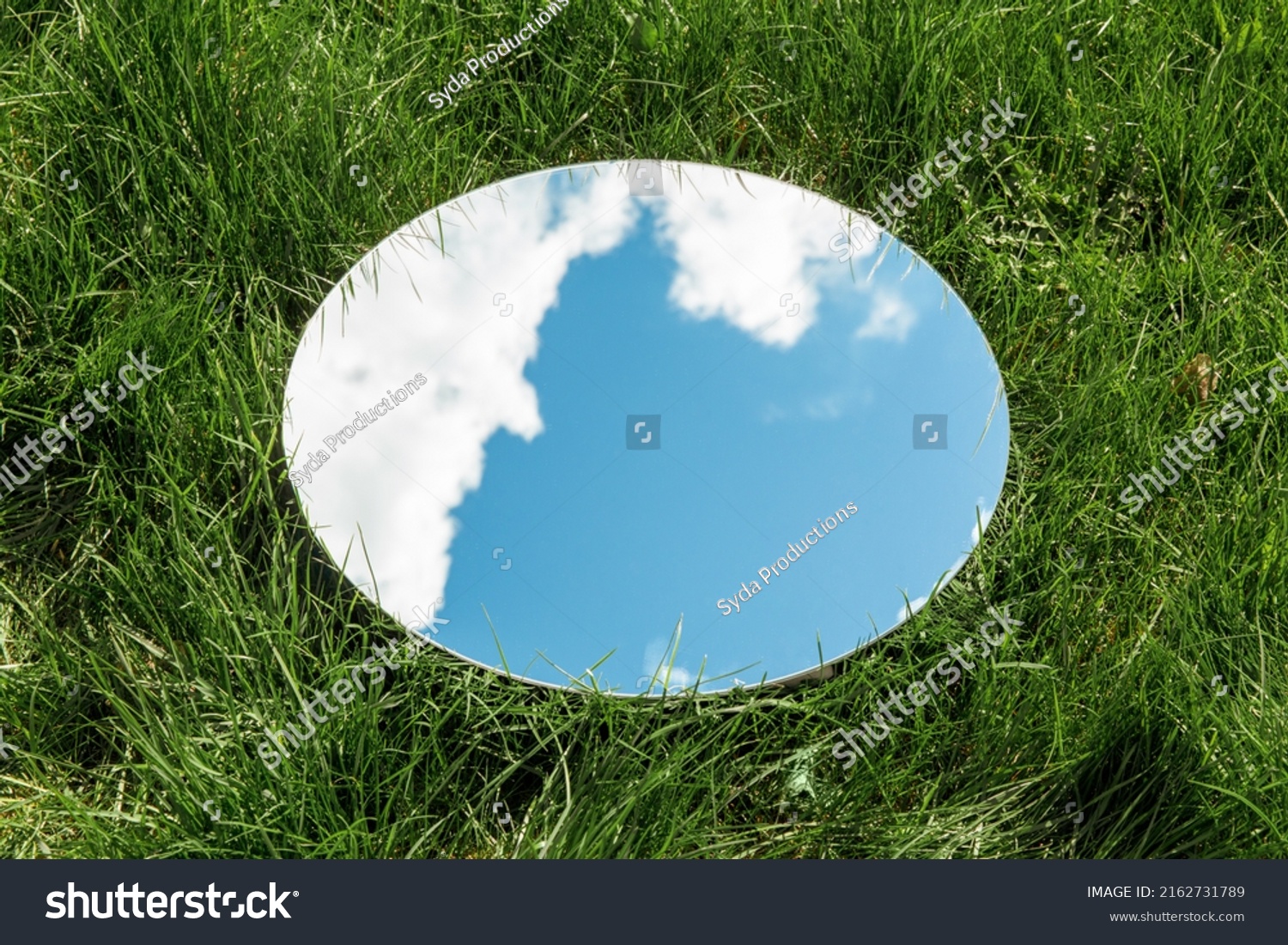 nature concept - blue sky and cloud reflection in round mirror on grass #2162731789