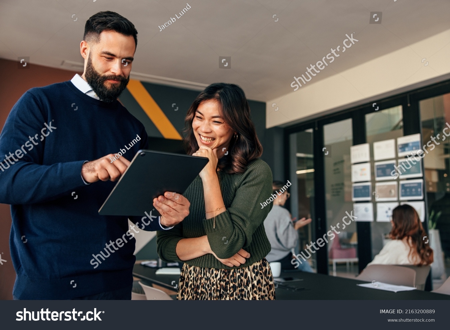 Happy business colleagues using a digital tablet in a boardroom. Two young businesspeople having a discussion during a meeting. Diverse entrepreneurs working together as a team. #2163200889