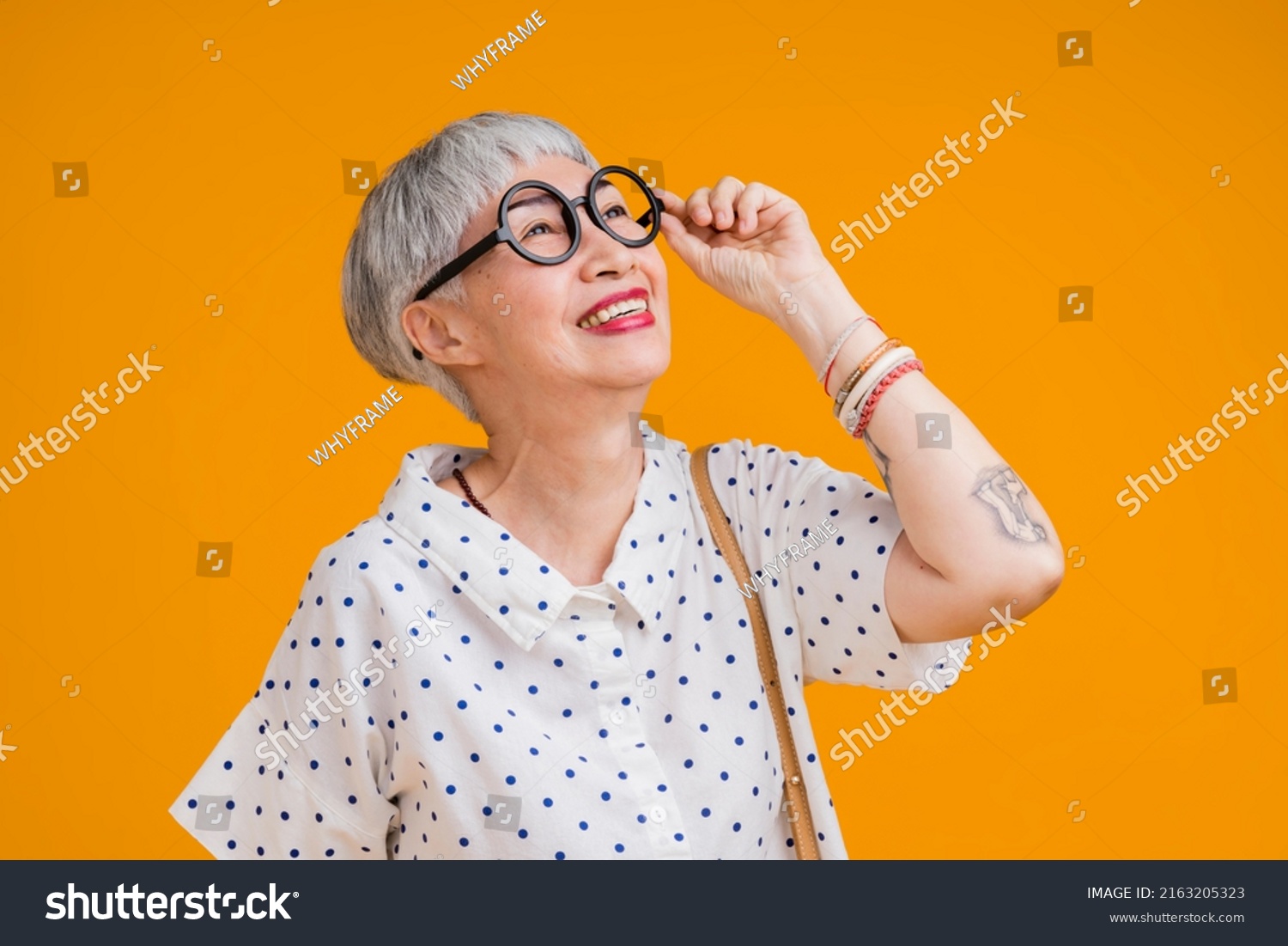 Portrait of attractive funky asian tattoo cheerful grey-haired elder old senior woman touching spectacles isolated over yellow pastel background color,surprise and over exited feeling expression #2163205323