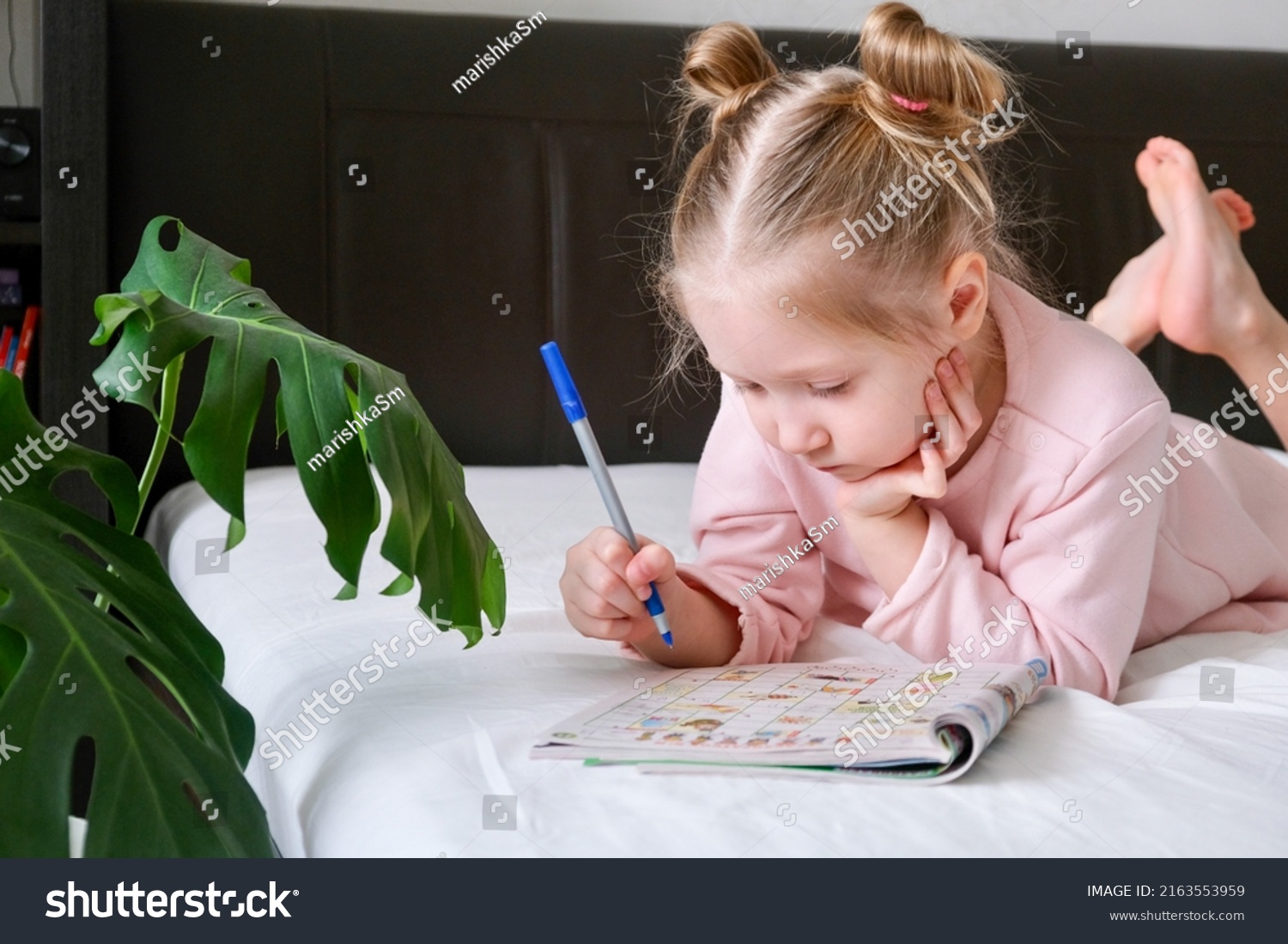 Portrait of a schoolgirl solves children crosswords on the bed. Logic games at home. solving crossword puzzles  #2163553959