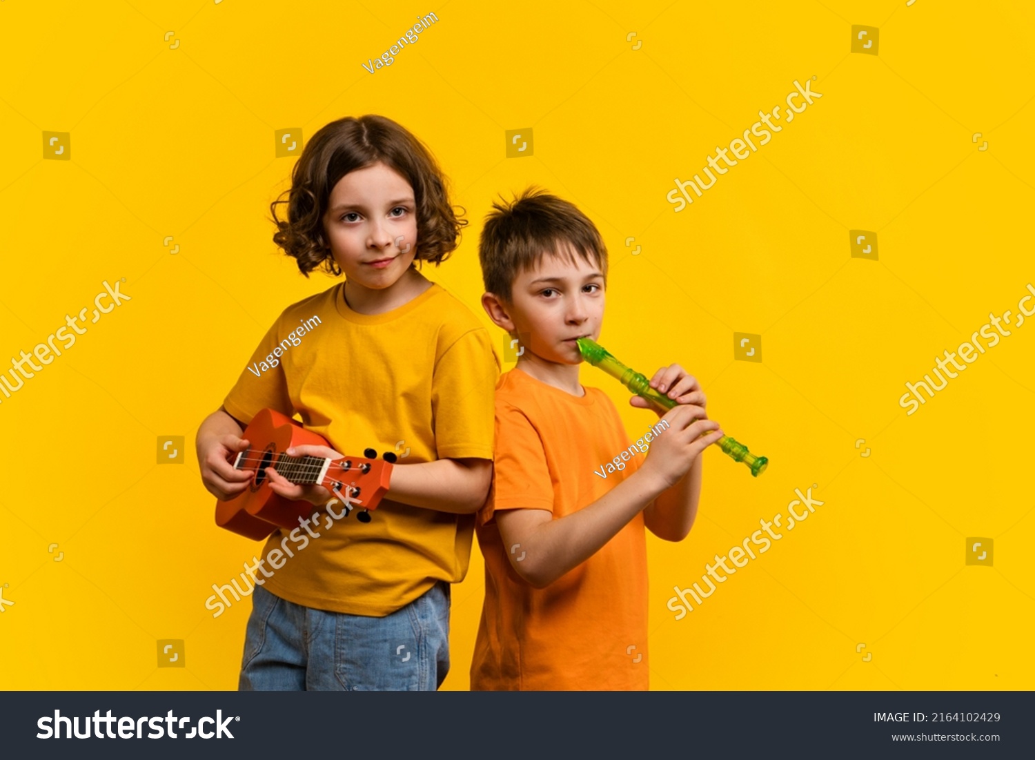 Musical duet in studio on yellow background. Child girl plays ukulele. School boy plays block flute. Two school children practice playing musical instruments #2164102429