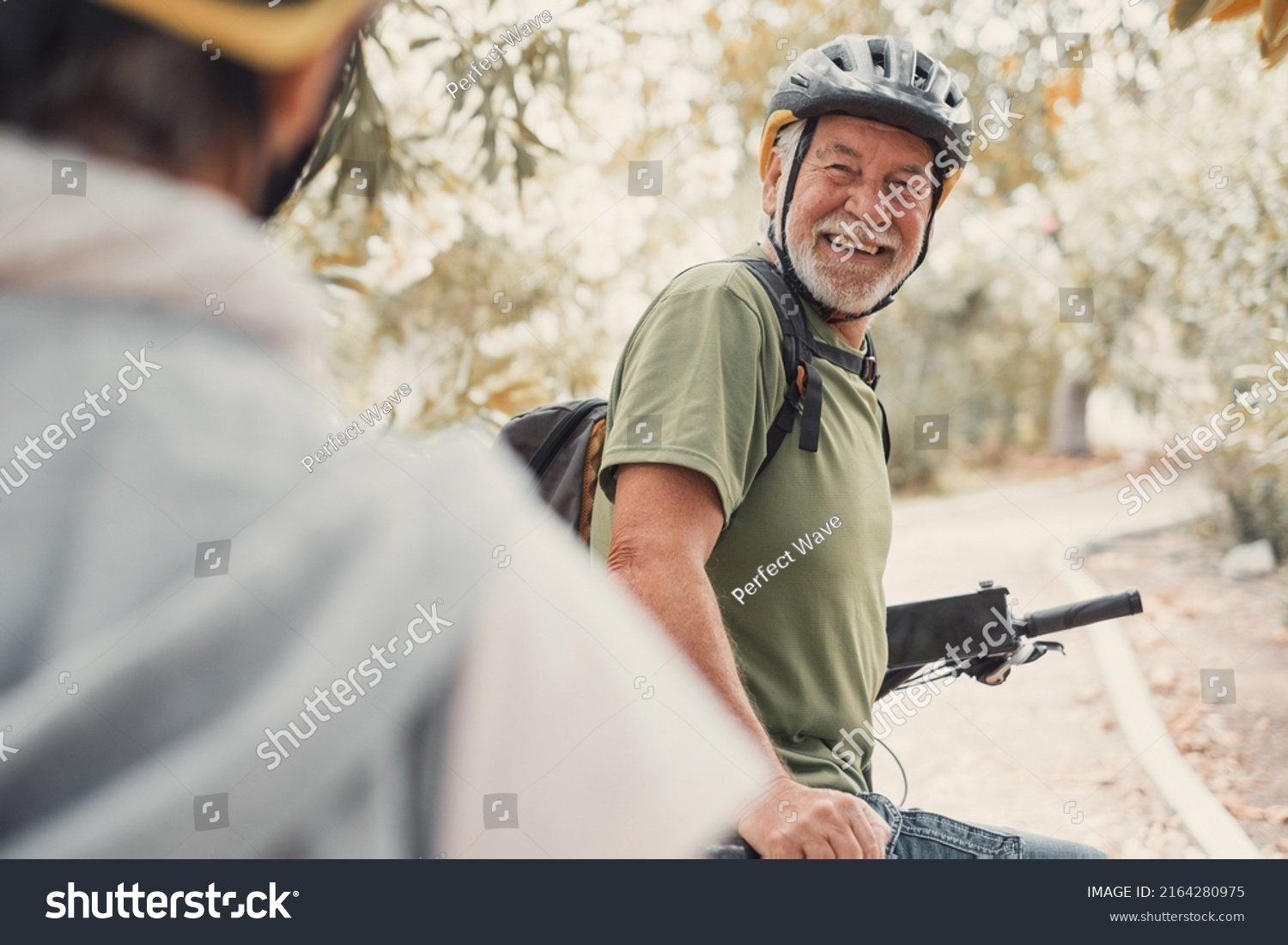 Two happy old mature people enjoying and riding bikes together to be fit and healthy outdoors. Active seniors having fun training in nature. Portrait of one old man smiling in a bike trip with wife #2164280975