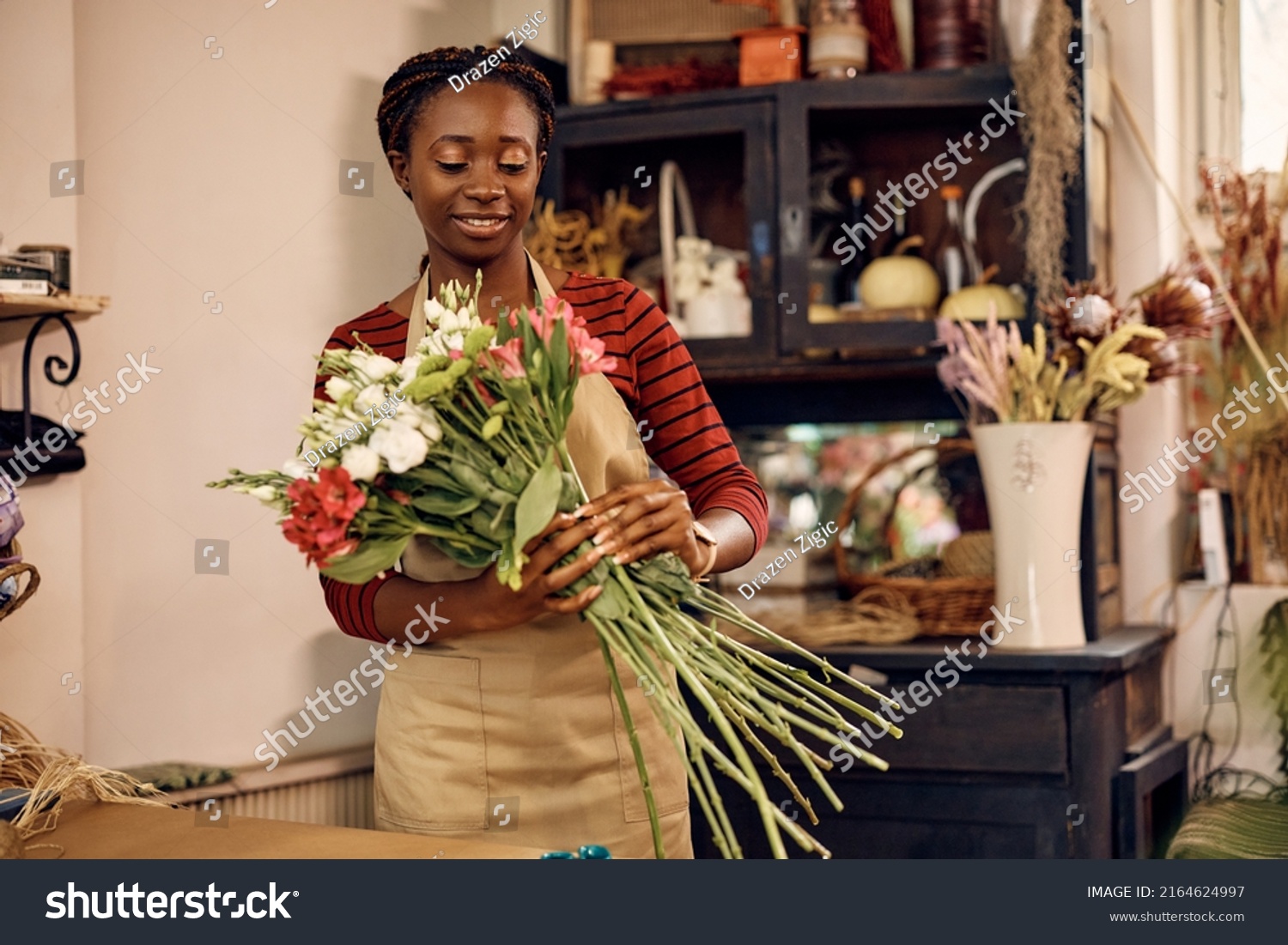 African American female florist making a bouquet of fresh flowers while working at flower shop. #2164624997