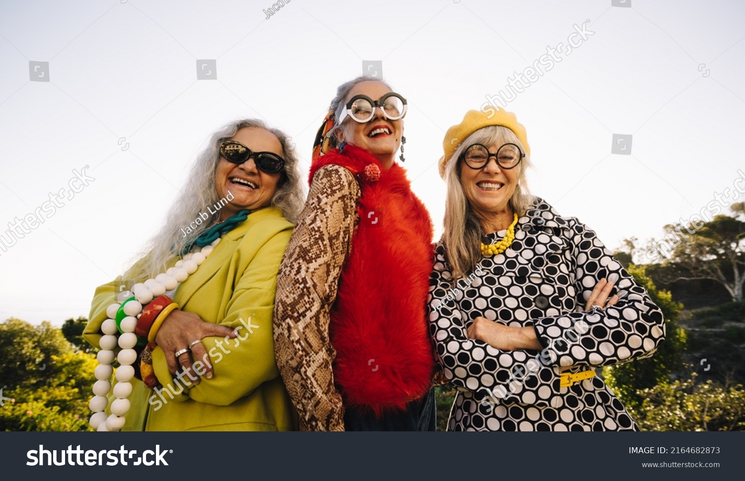 Stylish senior women smiling at the camera while standing together in a park. Group of confident elderly women wearing colourful casual clothing. Three mature women enjoying their golden years. #2164682873