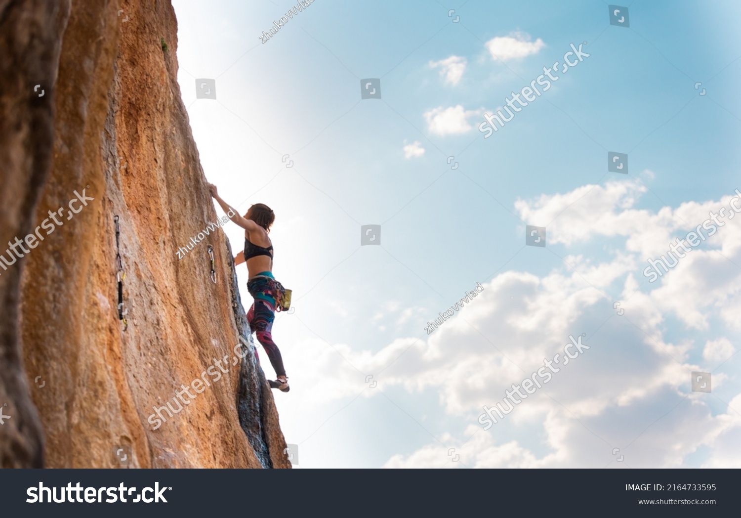 A woman climbs a rock against a blue sky, a strong girl trains strength and endurance, an extreme sport, rock climbing on natural terrain, a rock climber climbs with a rope #2164733595