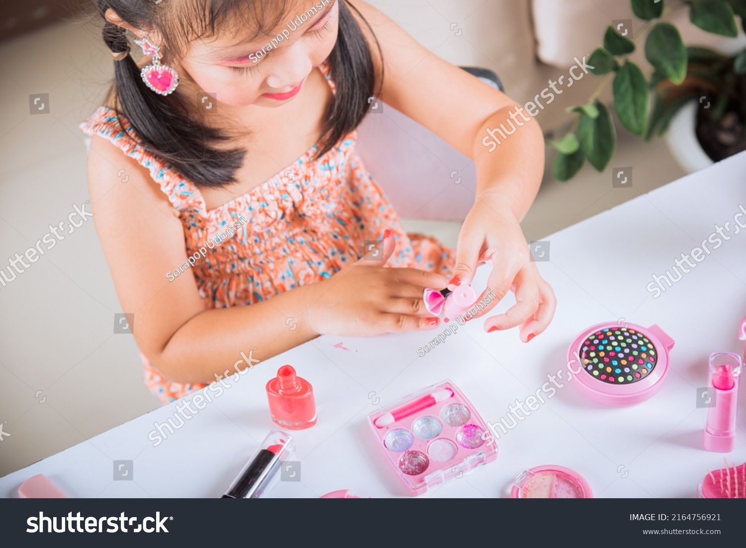 Asian adorable funny little girl making makeup dips brush into bottle to paints nails polish red nail varnish herself, Learning activity to be woman, happy kid is beautiful make up with cosmetics toy #2164756921
