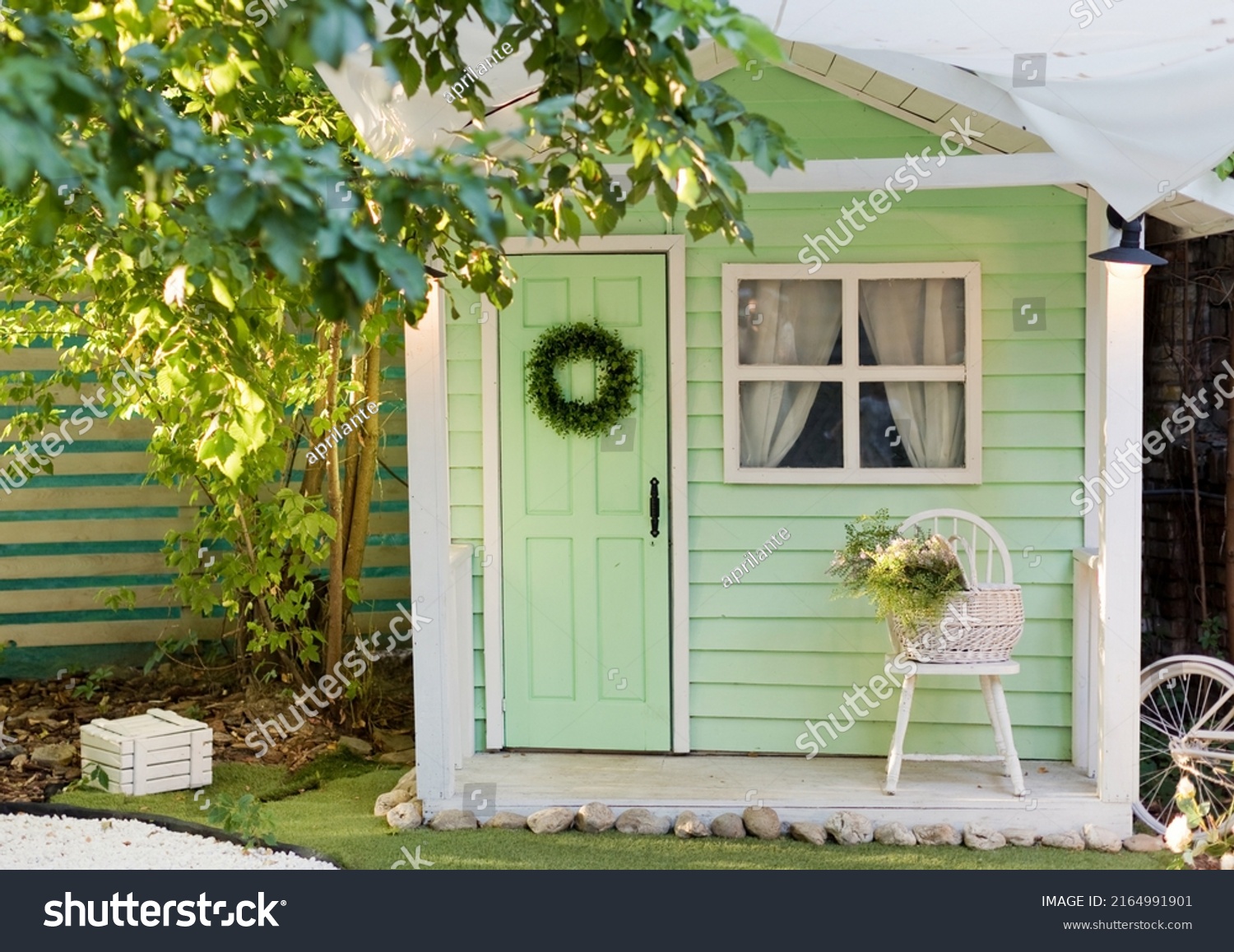Small green shed garden house with window, door and chair outside. Kids playhouse, garden summerhouse background #2164991901