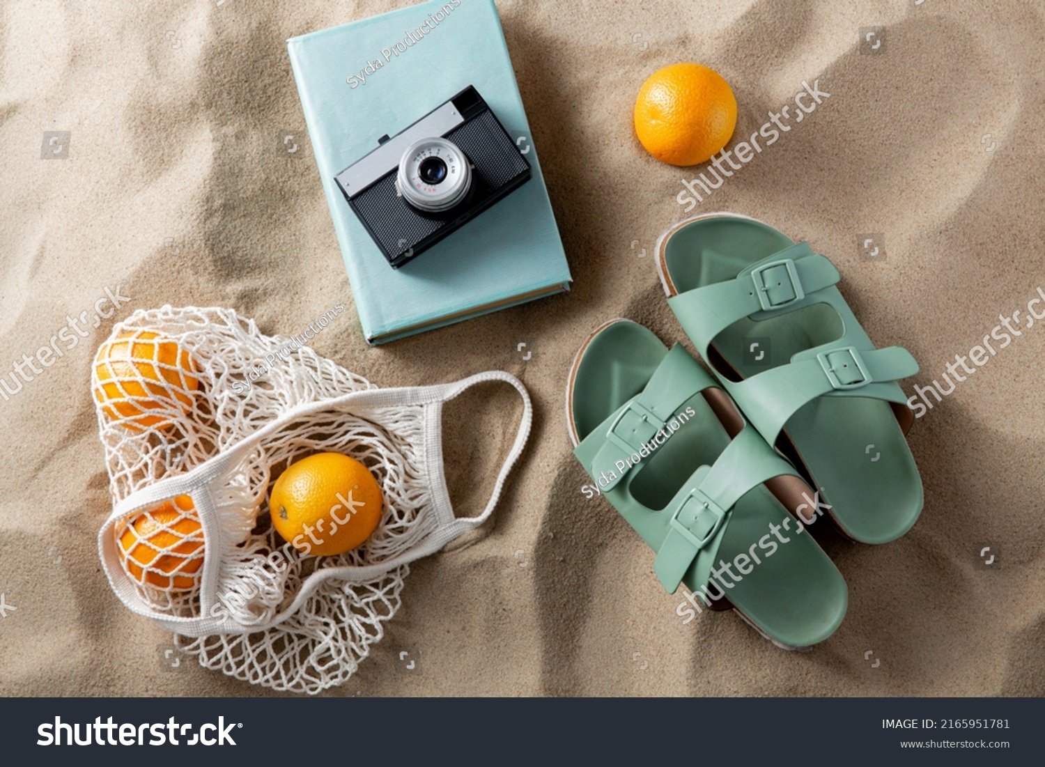 leisure and summer holidays concept - slippers, string bag of oranges, film camera and book on beach sand #2165951781