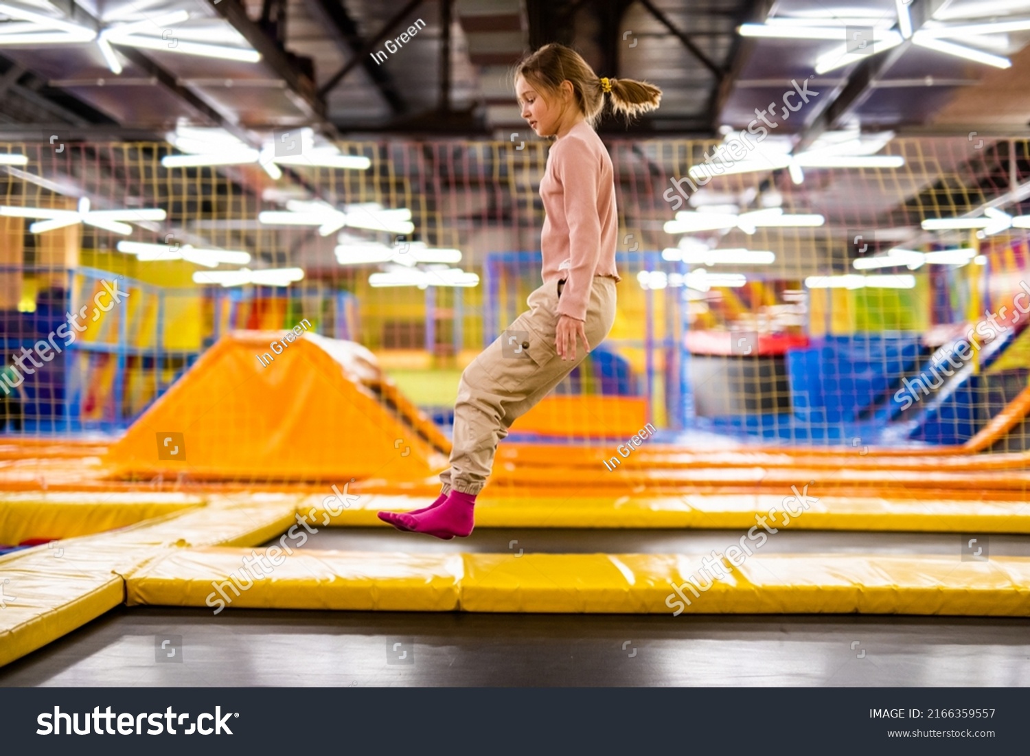 Cute girl kid jumping on trampoline and happy at playground park. Caucasian child in motion during active entertaiments #2166359557
