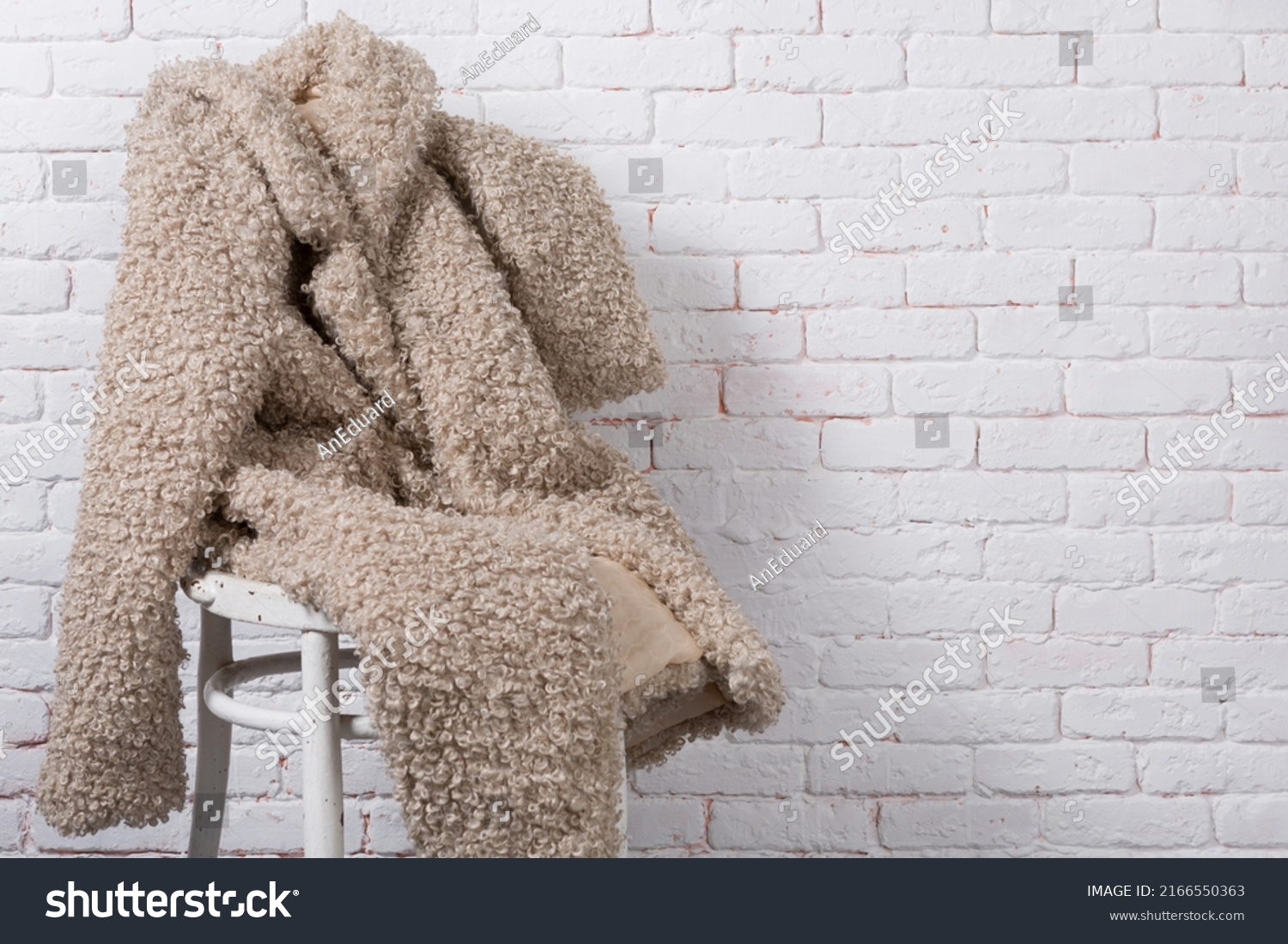 beige faux fur coat, as if sitting on a chair against a white brick wall, copy spase #2166550363