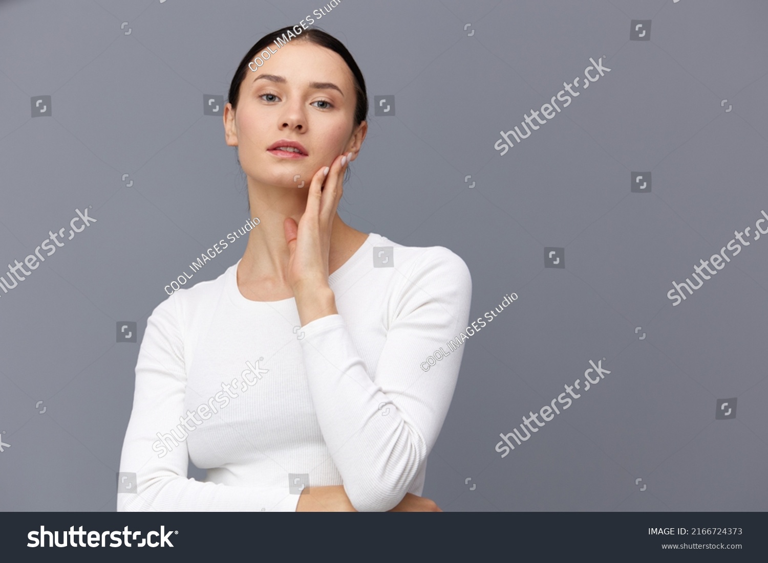 a cute woman with a ponytail on her head stands on a dark background in a white tight T-shirt, put her hand on her neck holding it with the other #2166724373