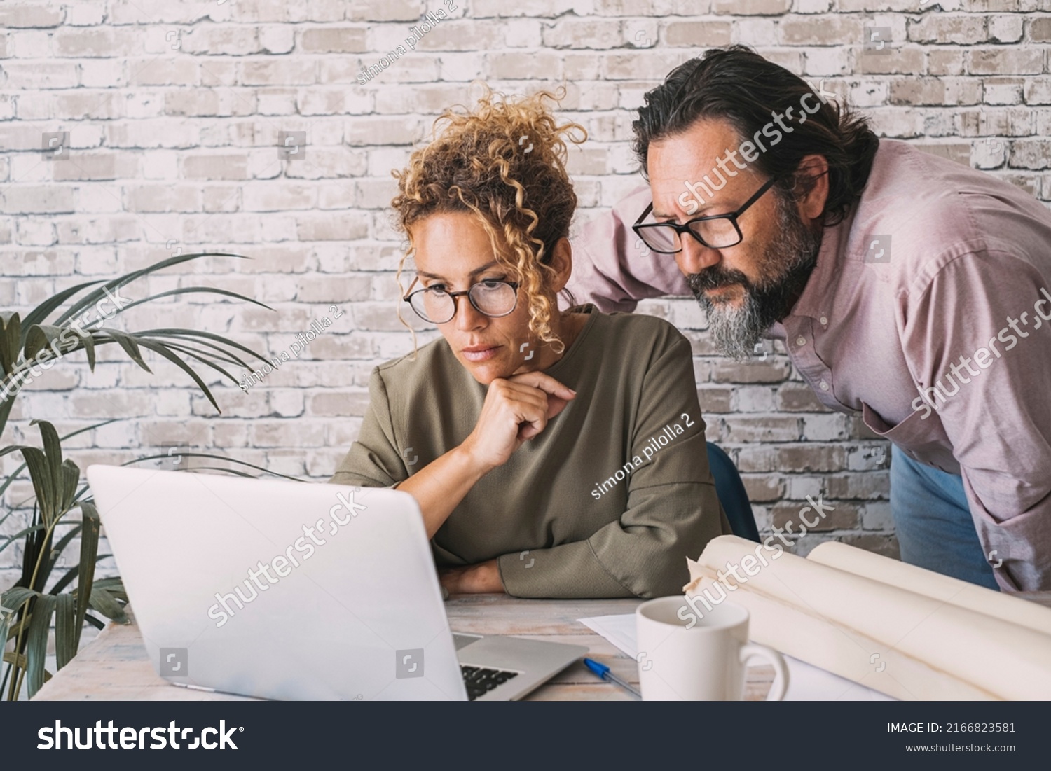 Man and woman working together on laptop in home office at the table desk. People and online digital job business. Adult couple looking with concentration on computer working. Concept of modern life #2166823581