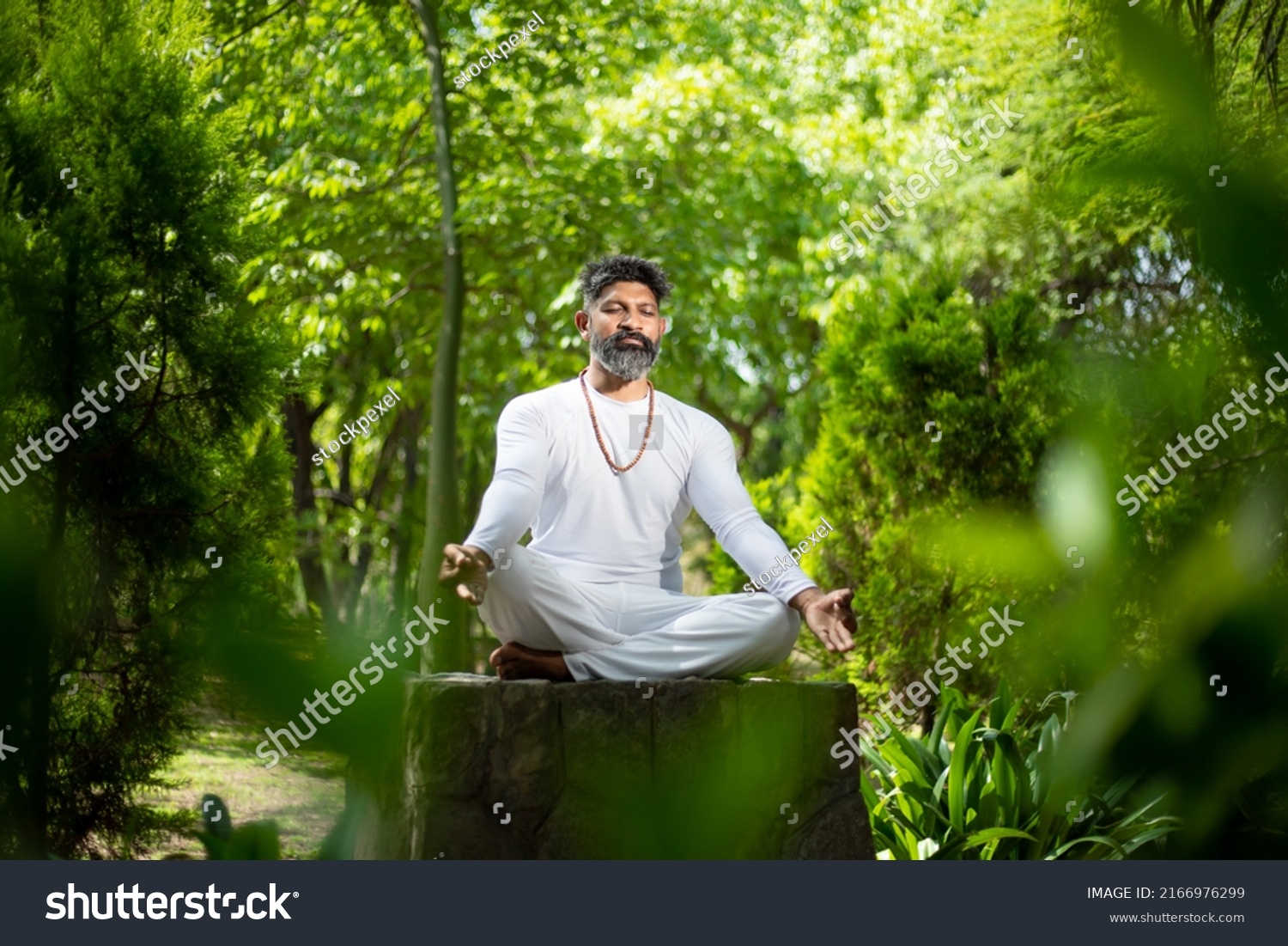 Indian man doing yoga meditation exercise in the green forest nature. fitness and yogi, healthy lifestyle. #2166976299