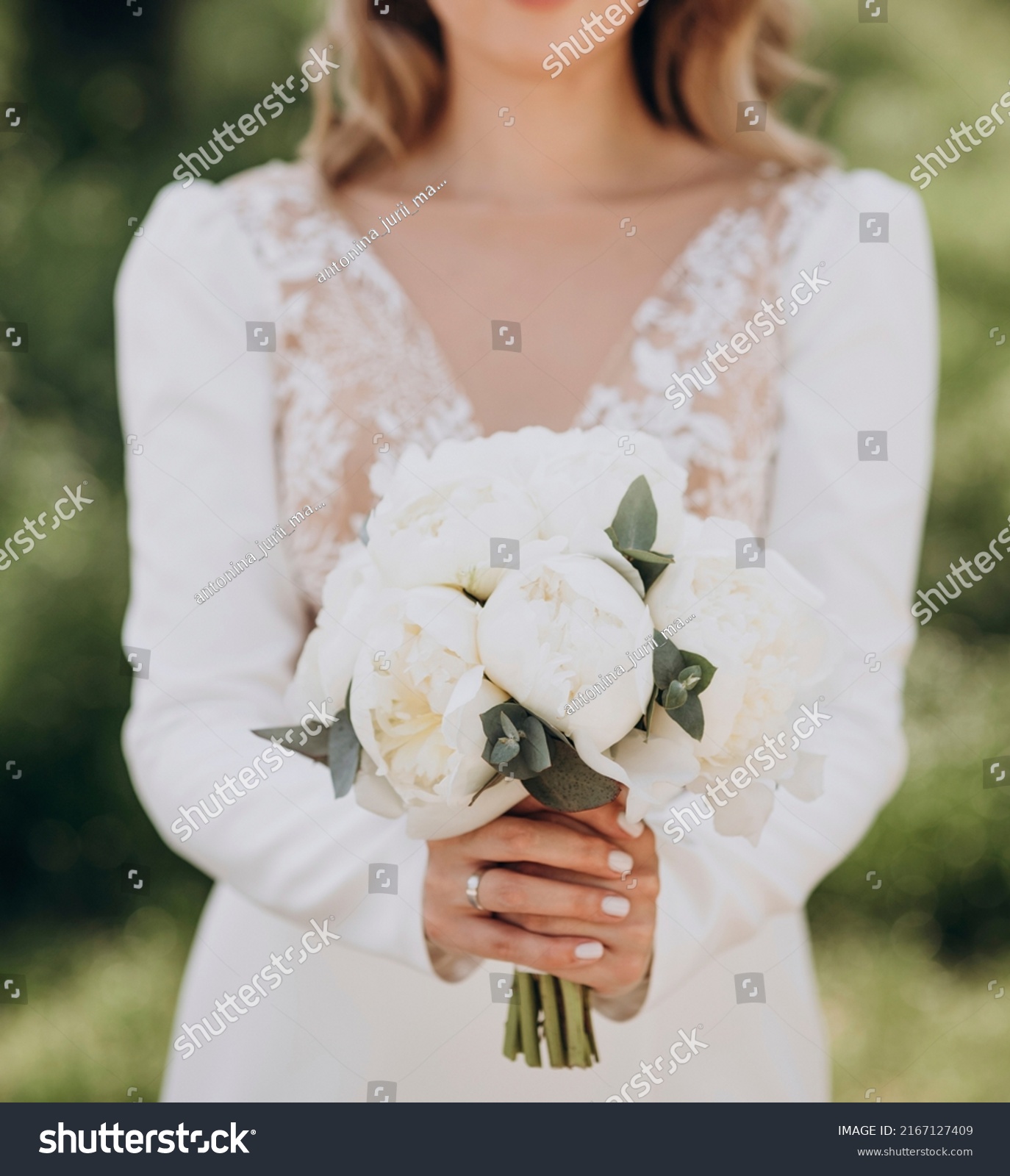 The bride in a white wedding dress is holding a bouquet of white flowers - peonies.. Wedding. Bride and groom. Wedding Dress #2167127409