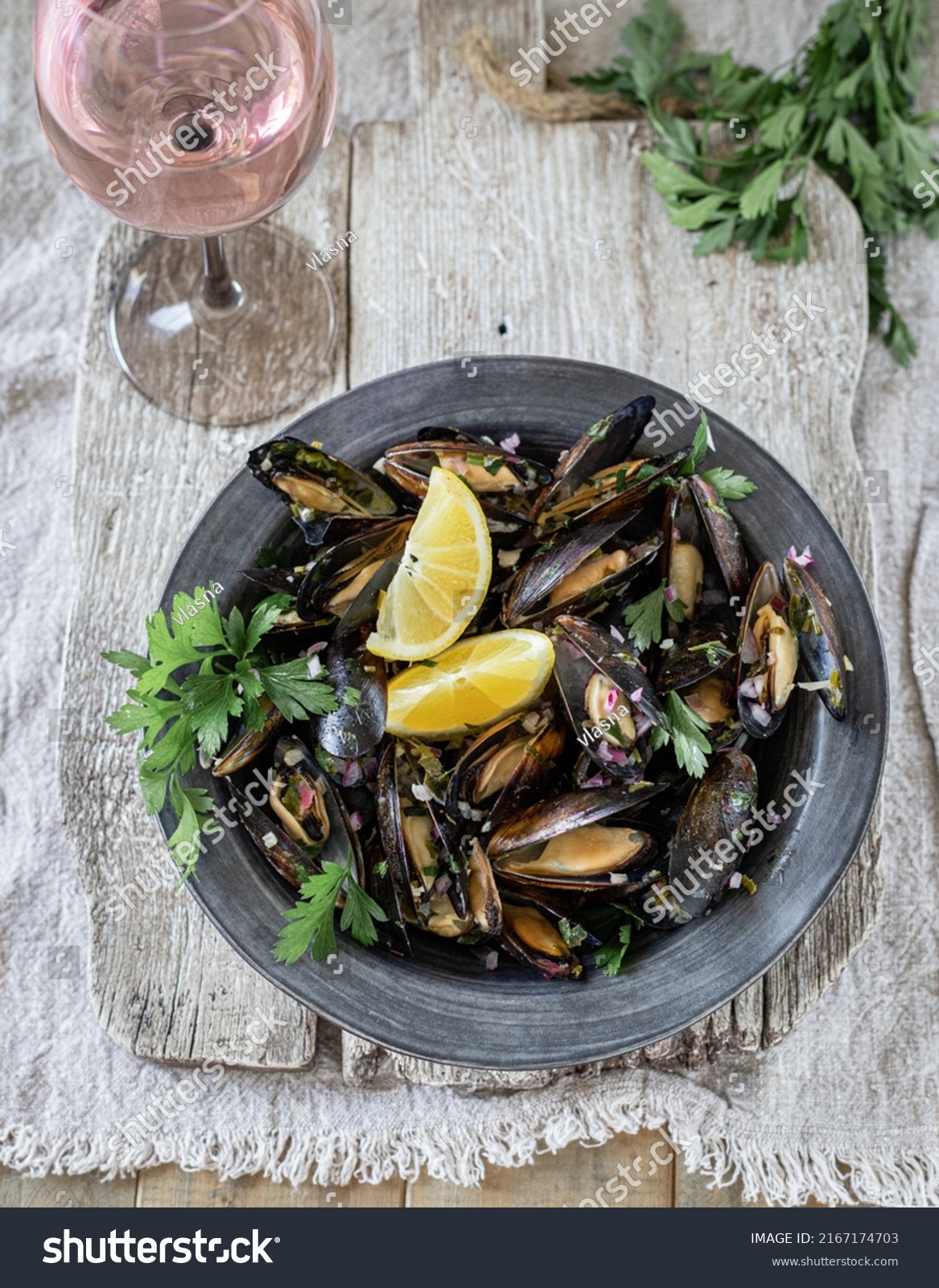 Mussels prepared with white wine, butter, garlic, lemon and herbs; served on a rustic black ceramic plate with rosé wine
Top view #2167174703