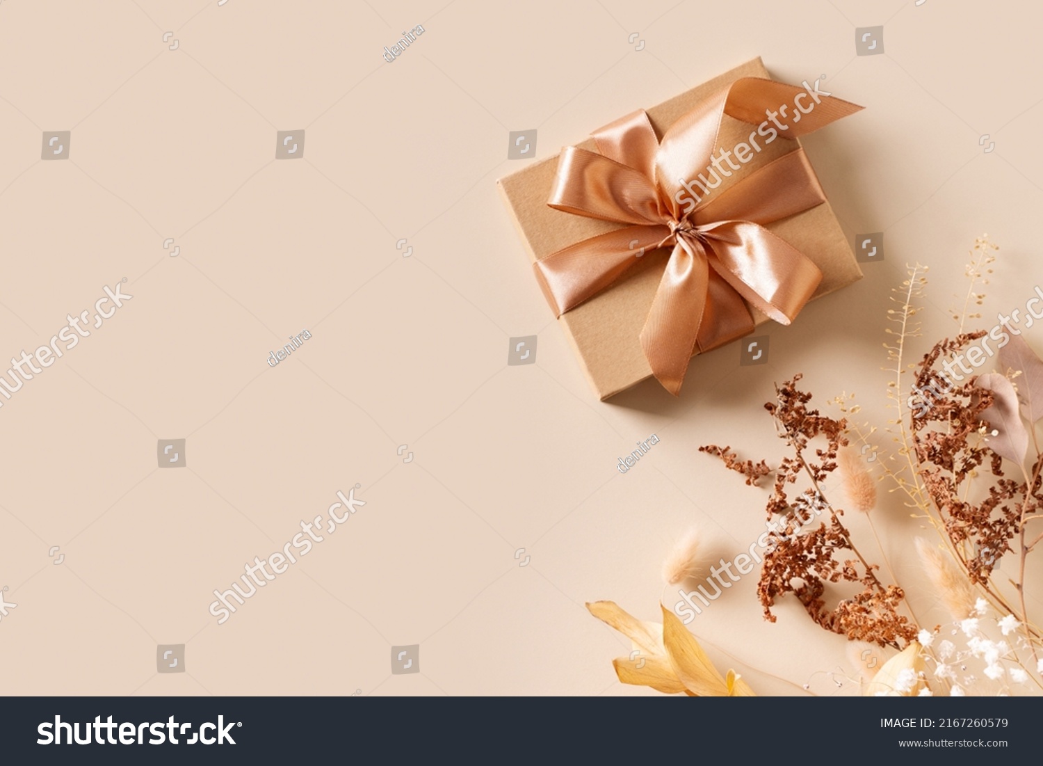 Gift box with golden ribbon and dry grass and flowers on beige background flat lay, top view, copy space #2167260579