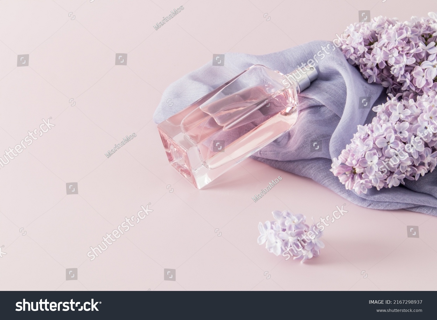 a chic bottle of women's perfume or eau de parfum lies on a woman's accessory - a scarf and lilac flowers. space for text. pink background #2167298937